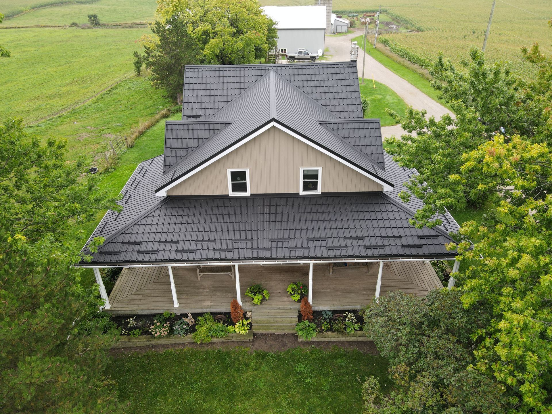An aerial view of a house with a black roof and a porch surrounded by trees.