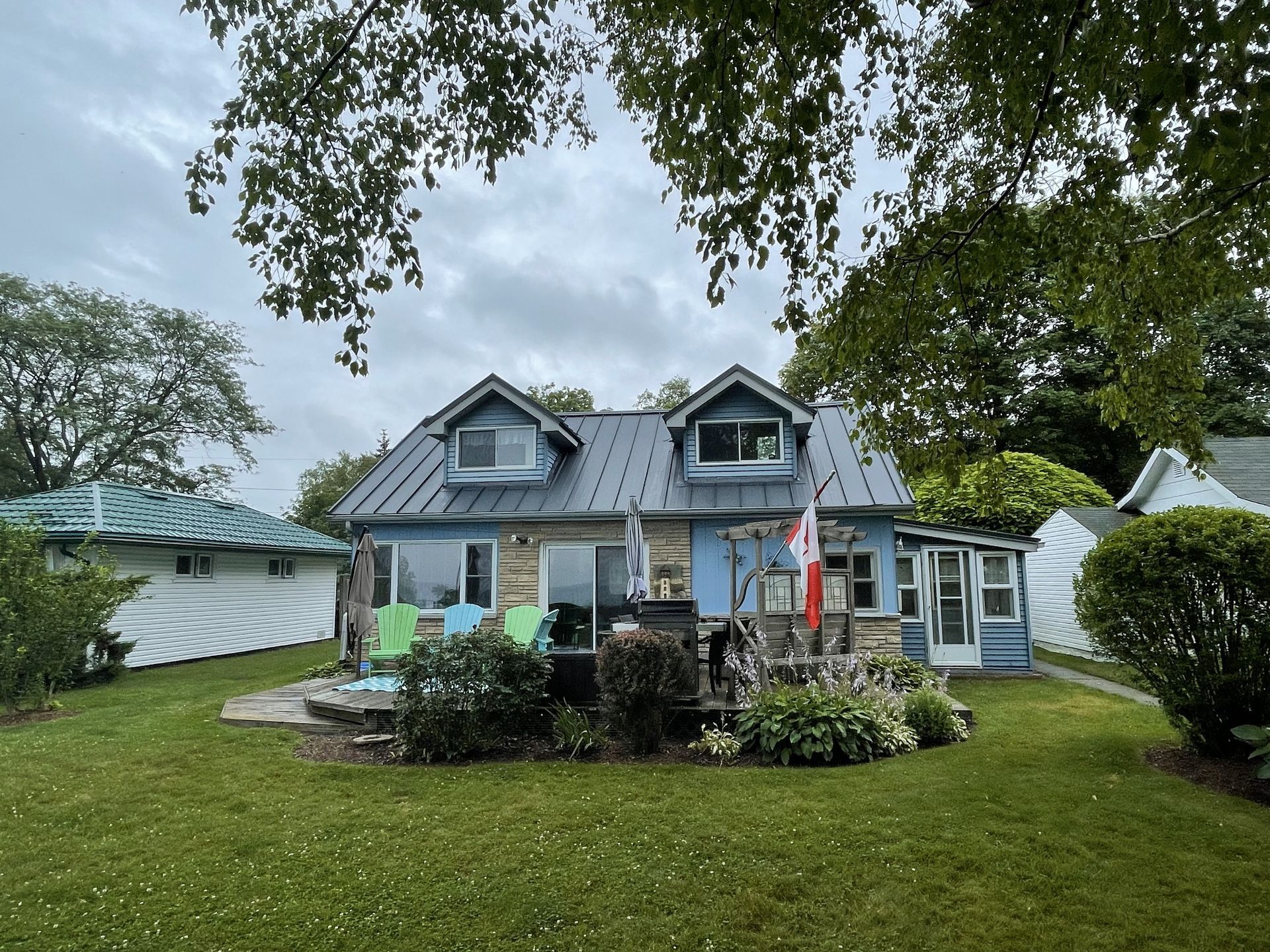 A blue house with a metal roof is surrounded by trees and grass.