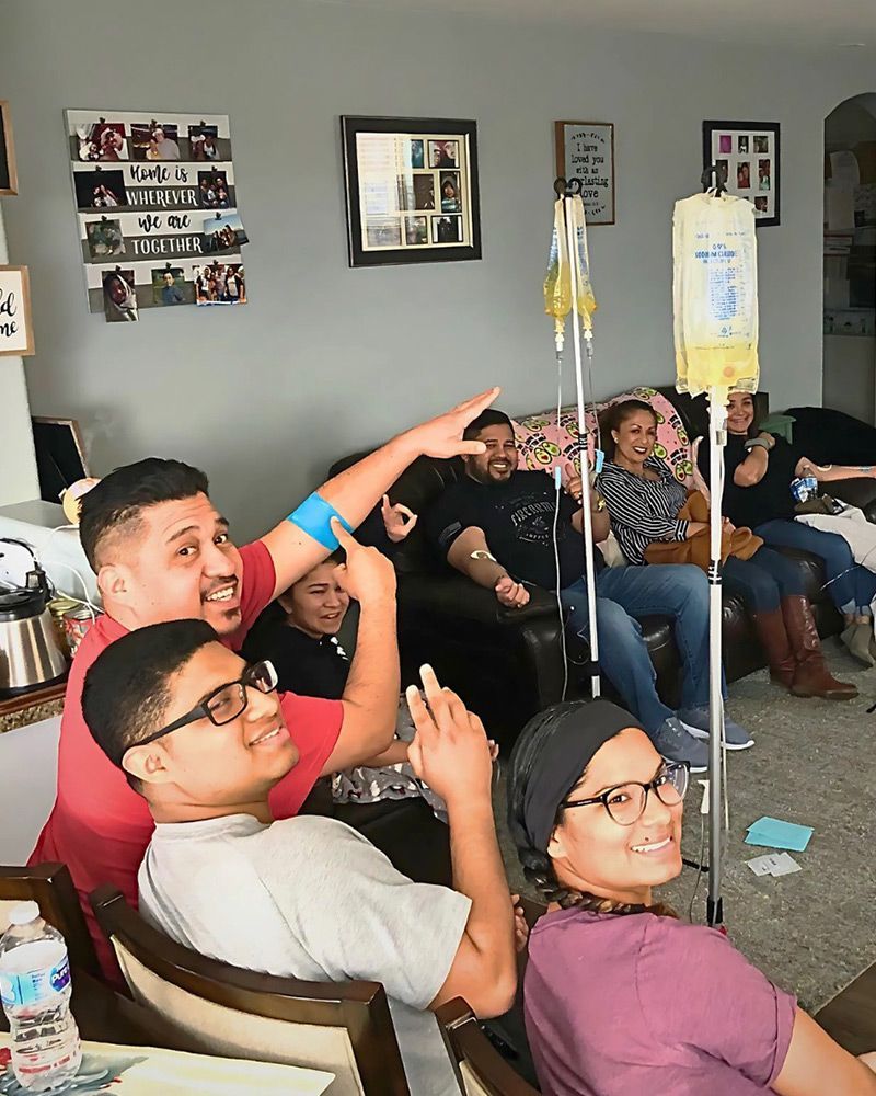A happy group of friends or family enjoying a mobile IV hydration party session in a living room, with yellow IV bags visible.
