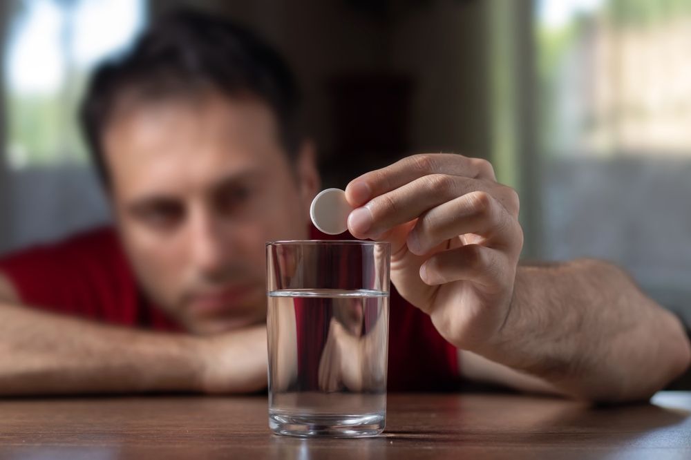 A man is taking a pill from a glass of water.