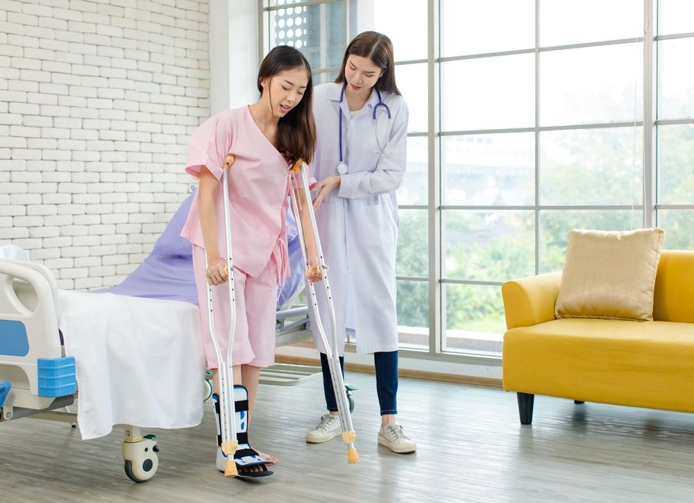 A doctor is helping a patient walk with crutches in a hospital room.