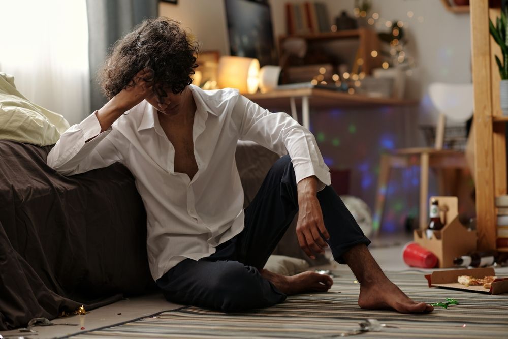 A man is sitting on the floor in a messy room.