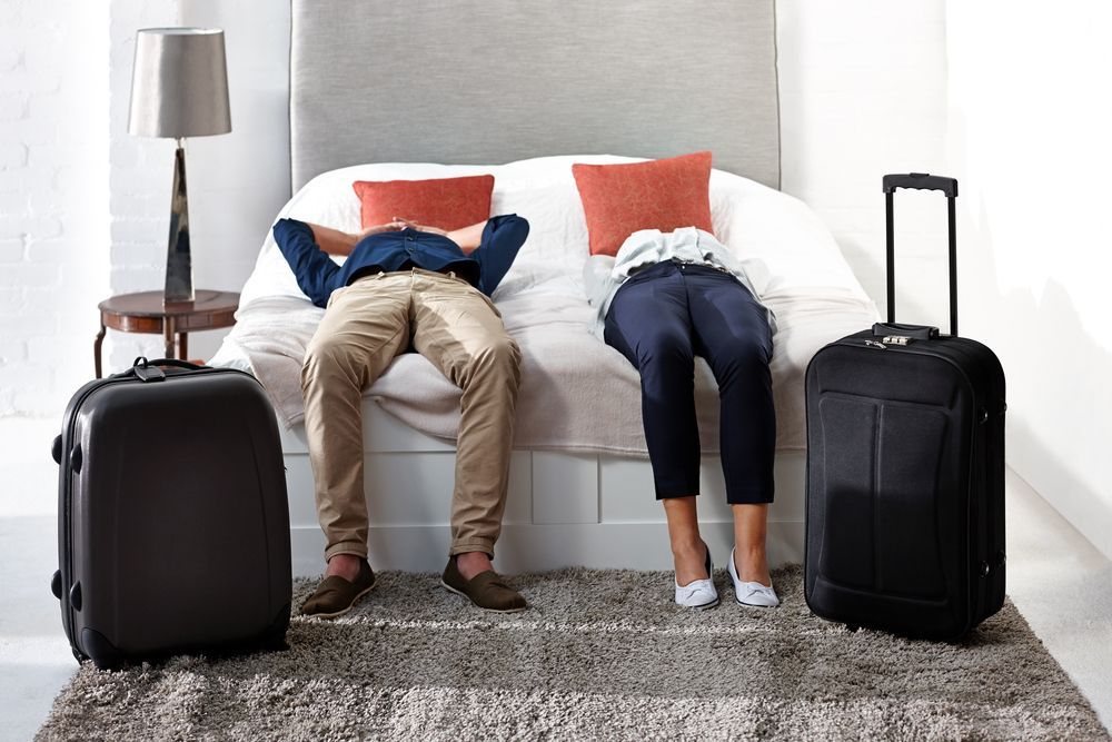 A man and a woman are sitting on a bed with luggage.