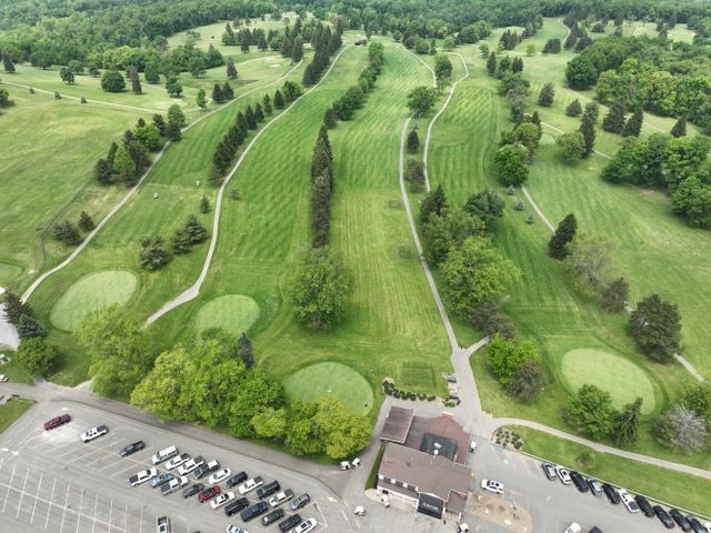Aerial view of a golf course featuring multiple fairways, greens, and a clubhouse with a large parking lot.
