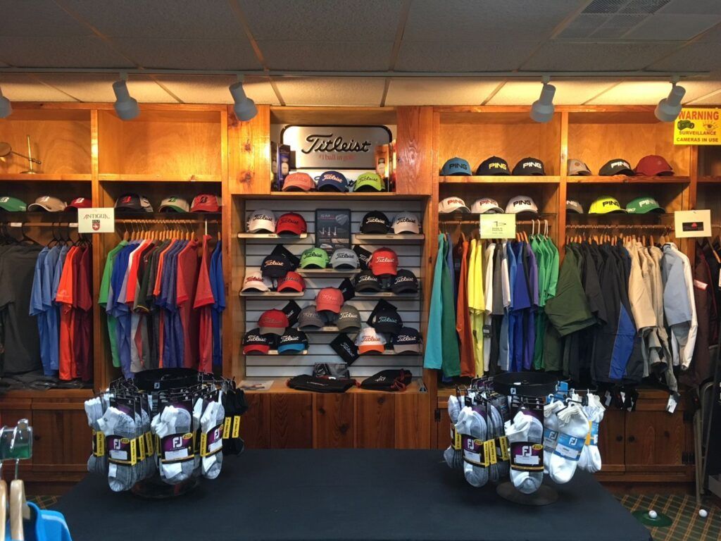 A golf pro shop with clothing racks, shelves filled with golf hats, and two displays of golf socks on a central table.