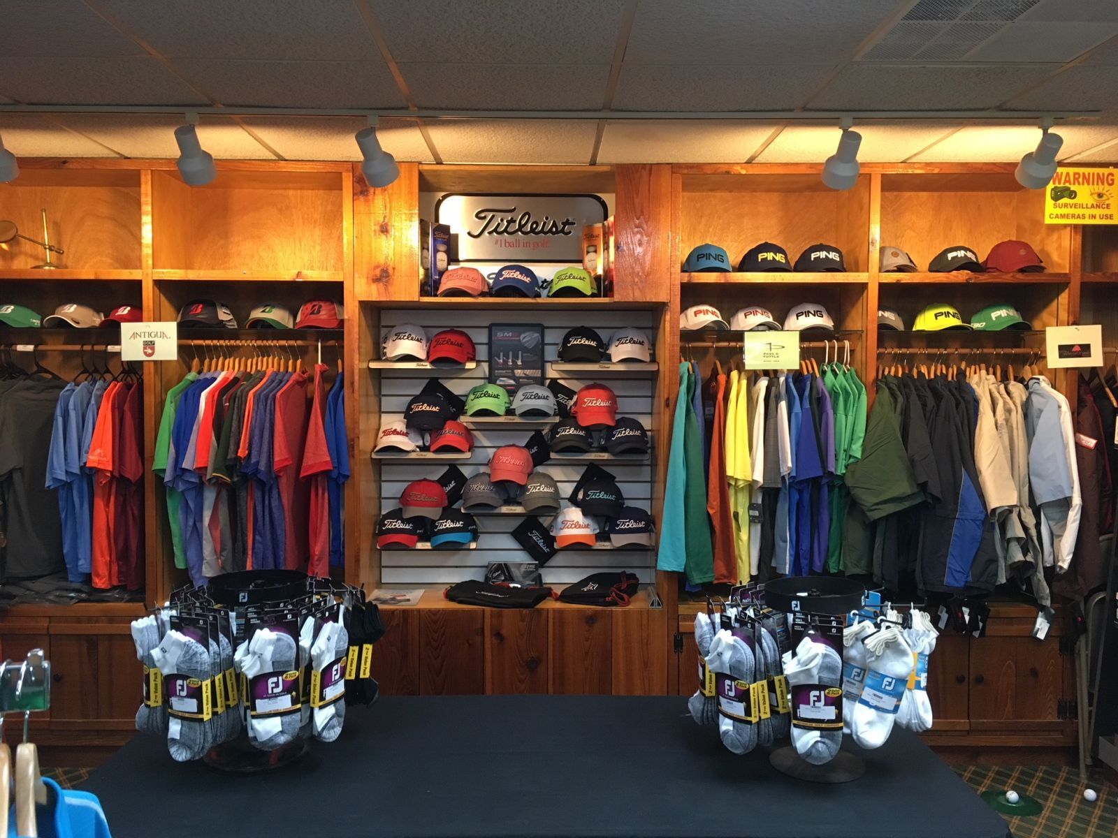 A golf pro shop with shelves of colorful caps and hanging shirts, featuring two circular racks of socks on a table.