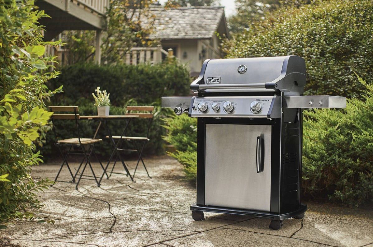 A stainless steel grill is sitting on a patio next to a table and chairs.