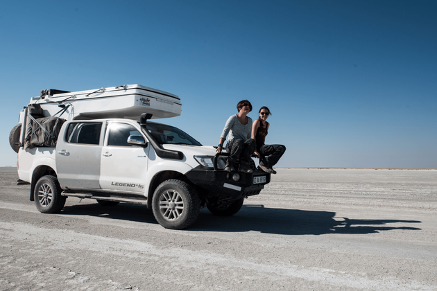 Stationery white 4x4 vehicle on a desert plain with two happy women sitting on the bull bar