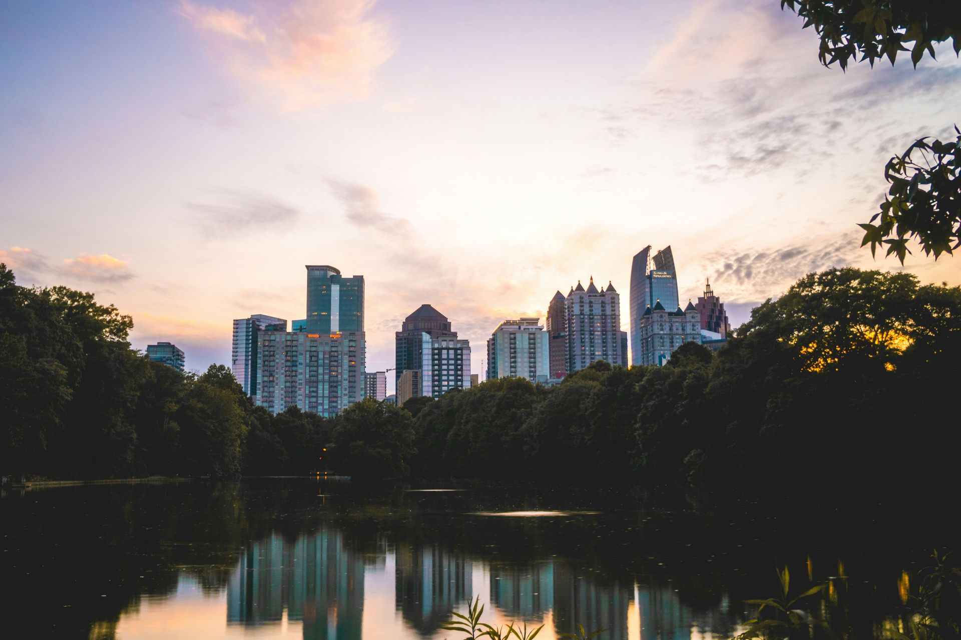 Atlanta skyline reflected in a calm park pond during a pastel-colored sunset.