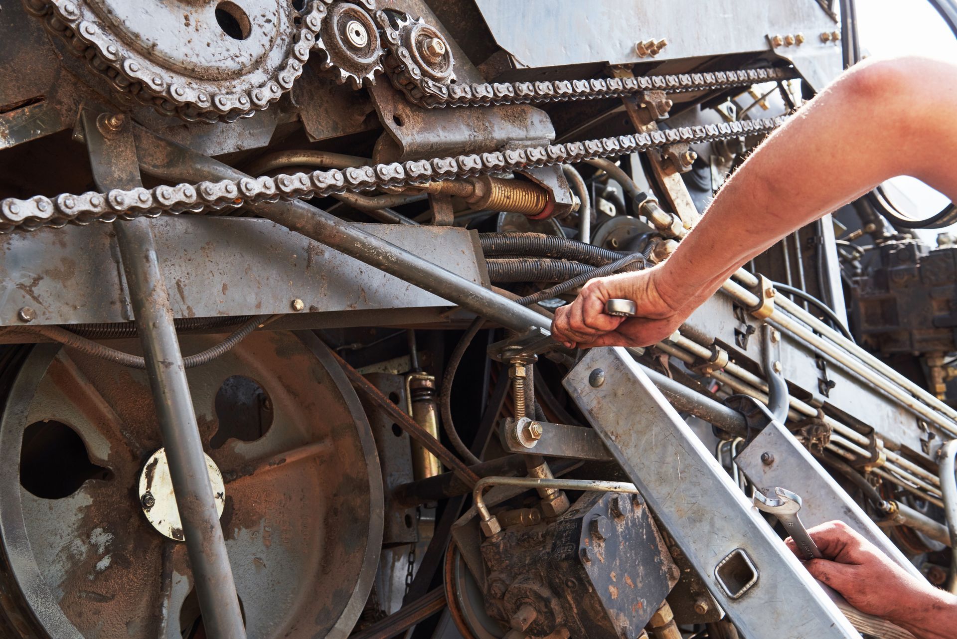 A close-up view of hands working on the intricate chain and gear mechanism of industrial machinery.
