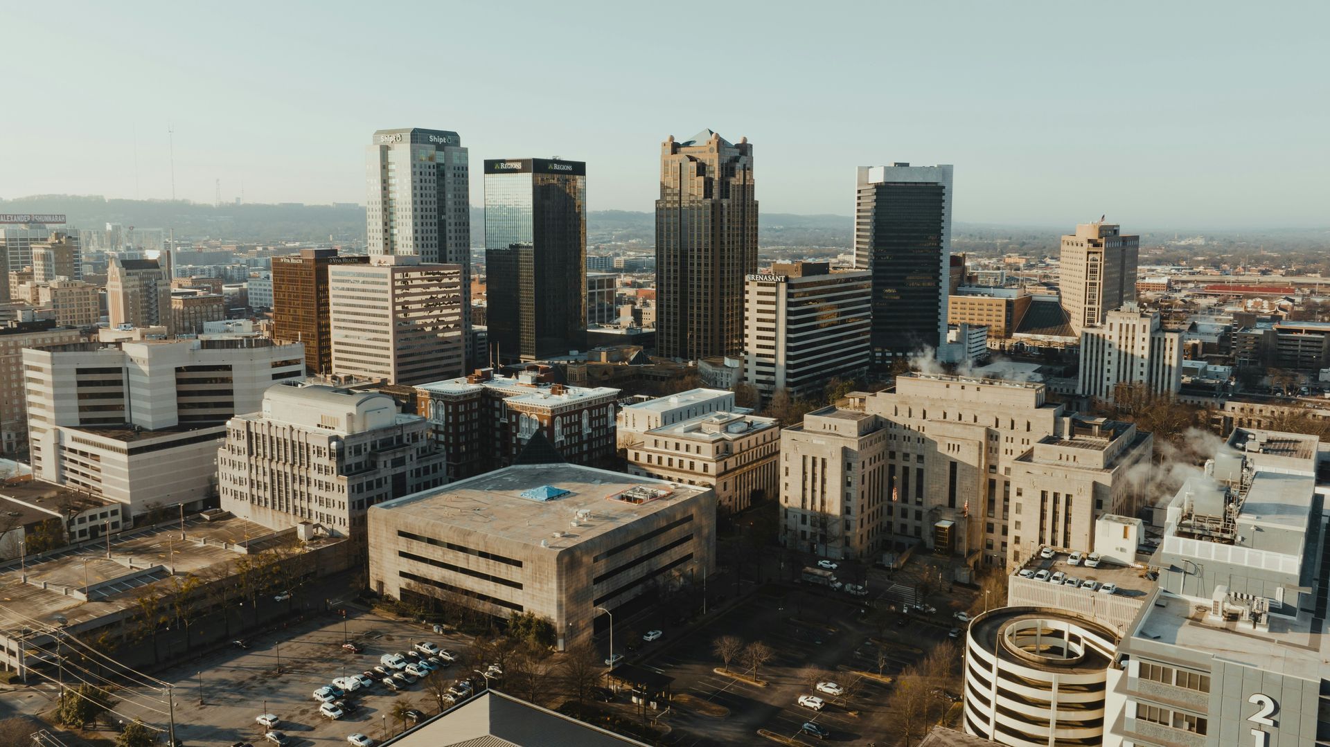 An aerial view of a city skyline with various skyscrapers, office buildings, and parking structures under a clear sky.