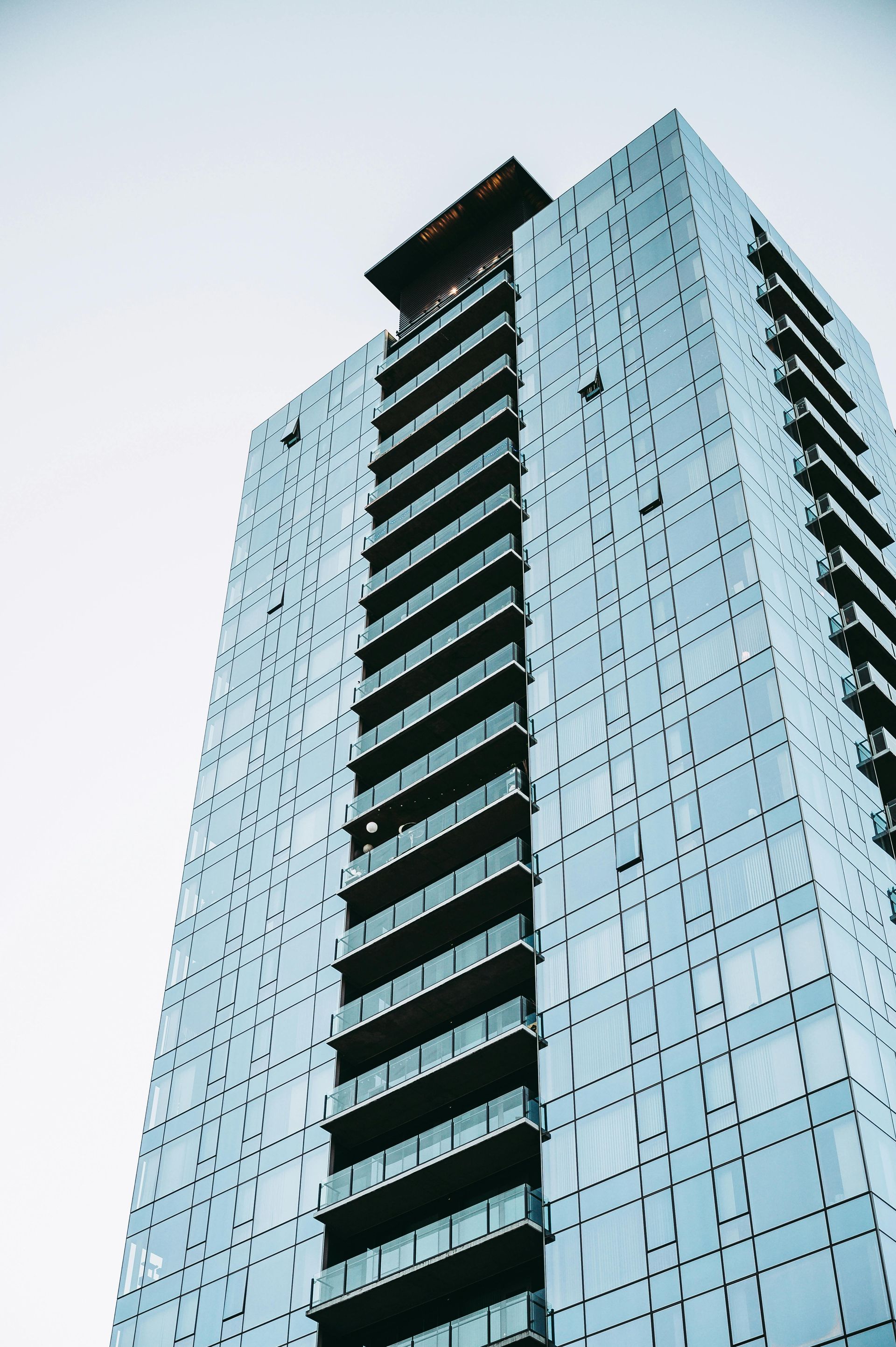A modern, glass-paneled skyscraper with a central column of recessed balconies rising against a pale sky.