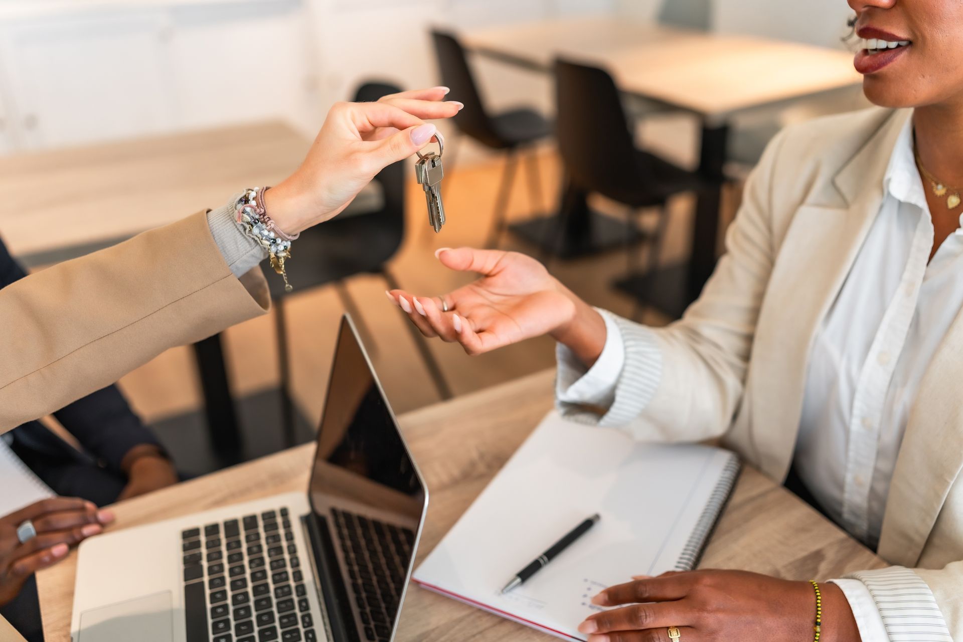 Two people exchange a set of keys over a desk with a laptop and documents, signaling a successful business transaction.