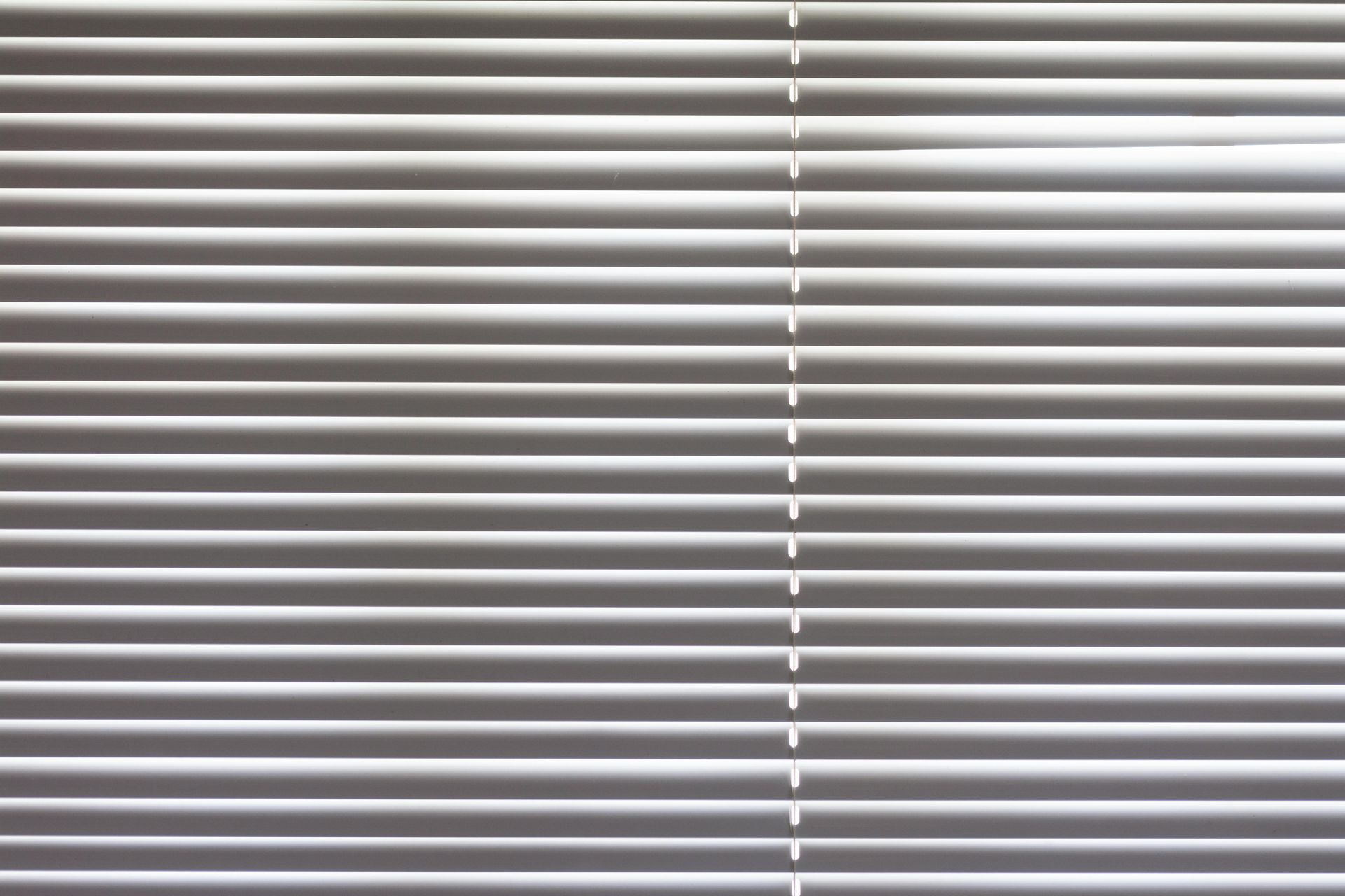 Graue horizontale Fensterjalousien mit gleichmäßig verteilten Lamellen.