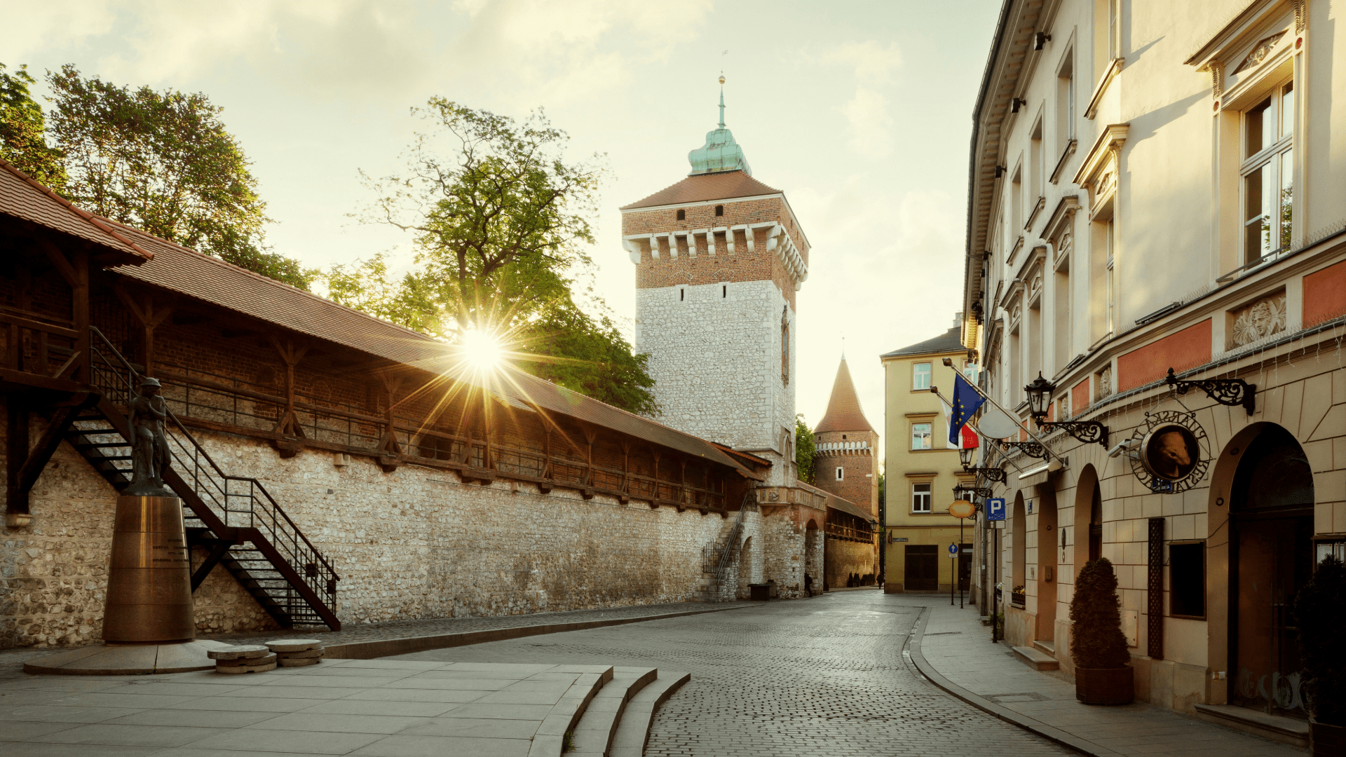 Sunlit street in Kraków’s Old Town featuring medieval city walls and a historic tower