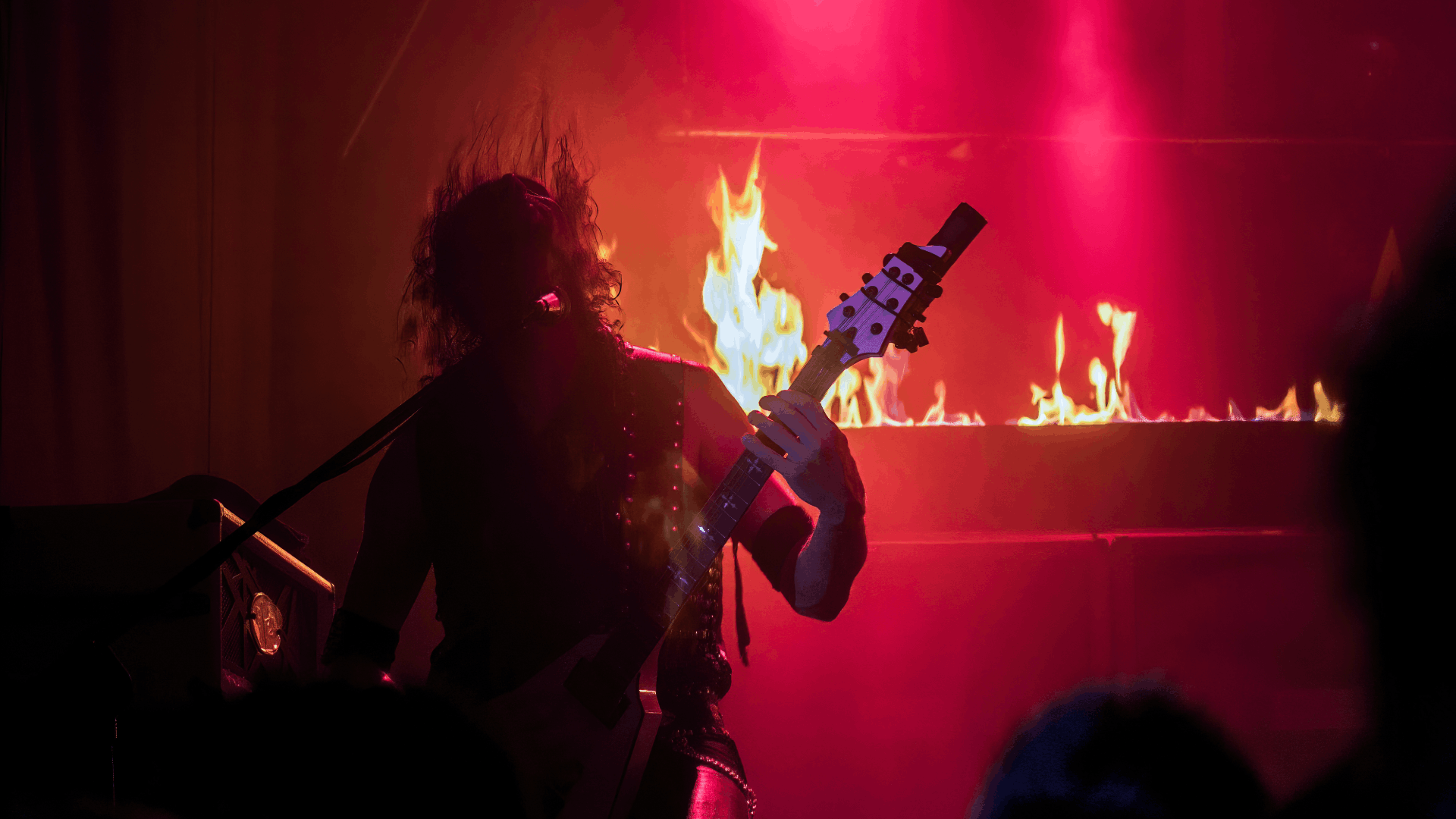 Live concert scene in blue stage lighting with a silhouetted musician and cheering crowd.