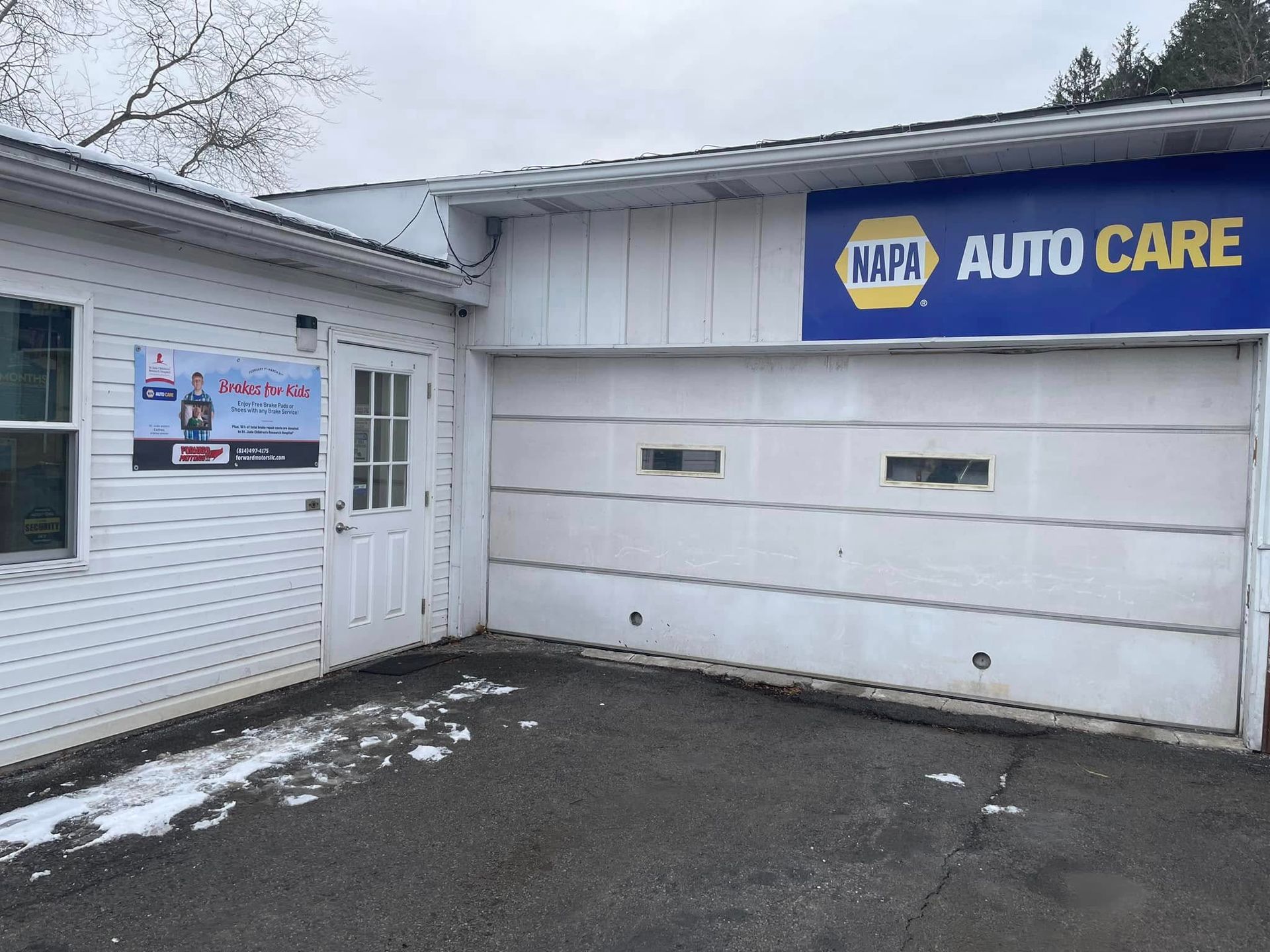 Exterior of a NAPA Auto Care shop with a closed garage door and a sign. | Forward Motors