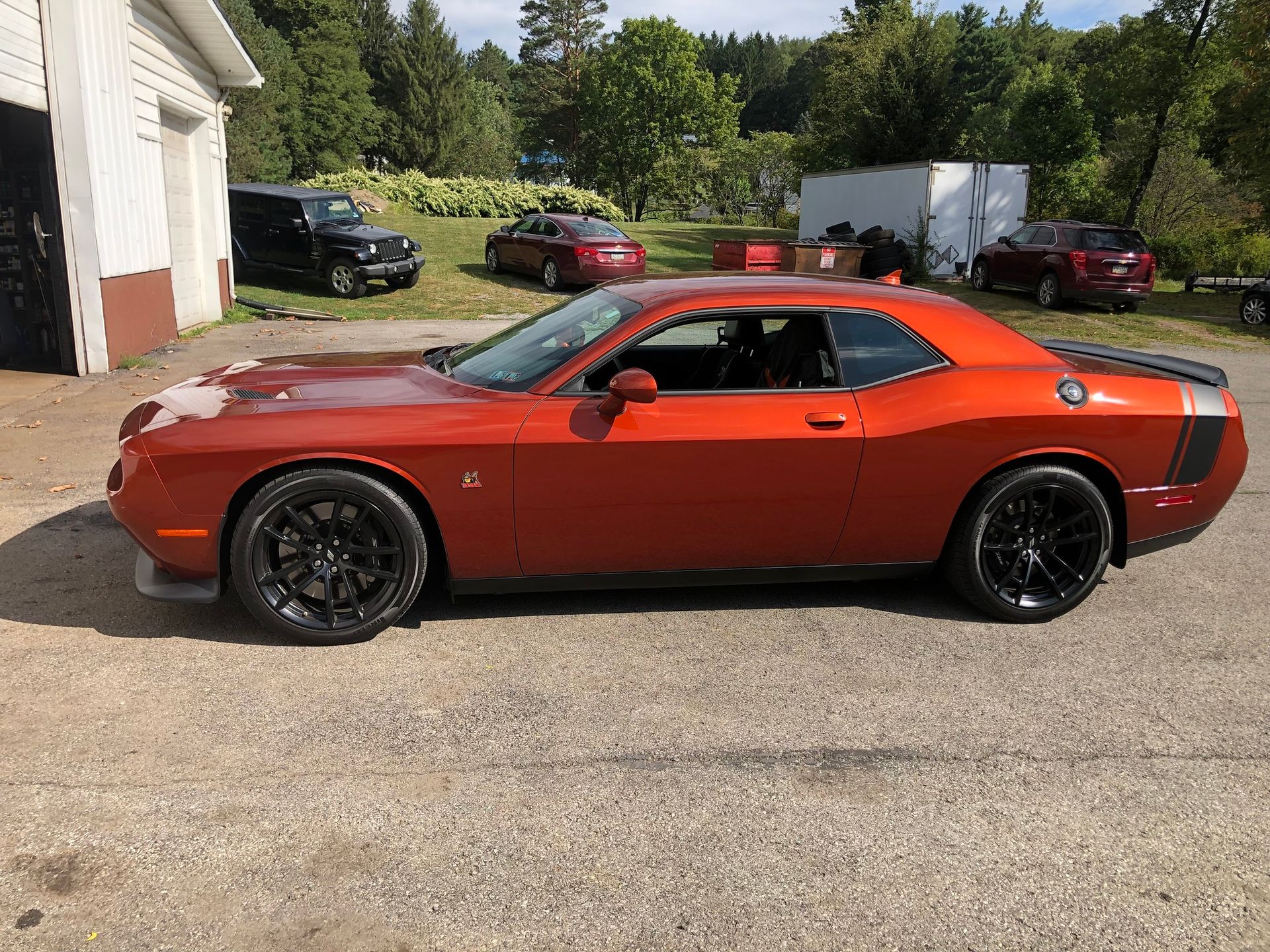 Orange Dodge Challenger parked on gravel, with other vehicles and a building in the background.