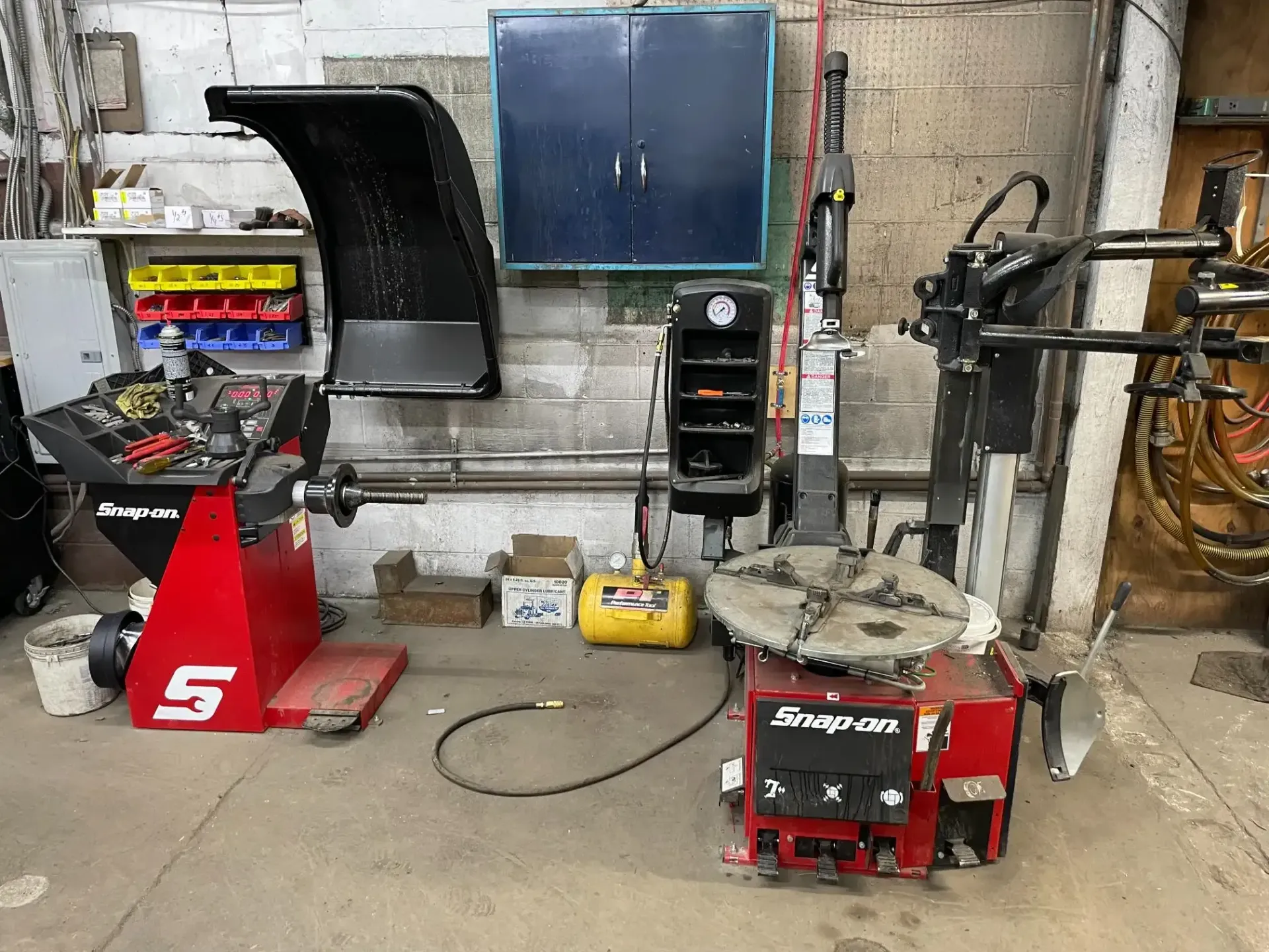 A tire shop with red Snap-on equipment, including a balancer and tire changer, against a brick wall.