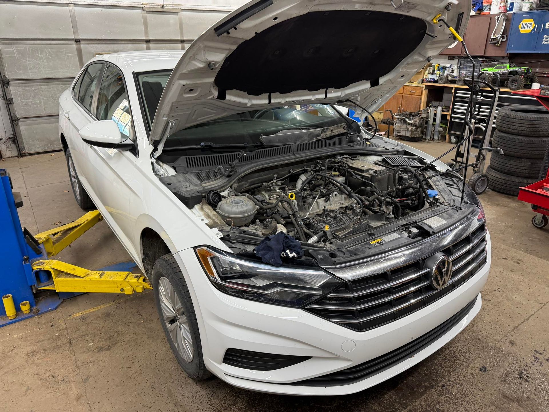 White car with open hood on a lift in a repair shop.