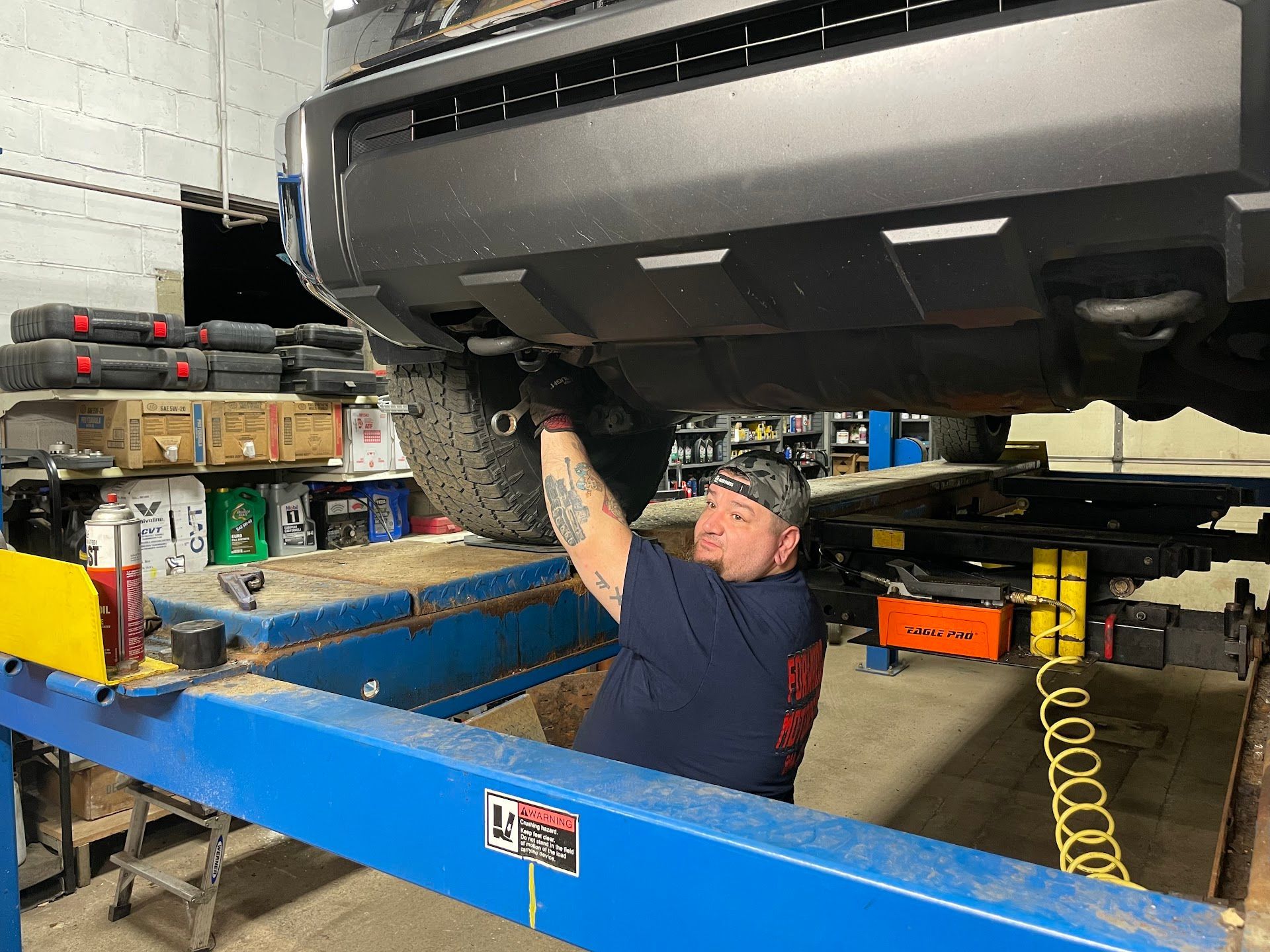 Mechanic working under a vehicle on a lift in a garage.