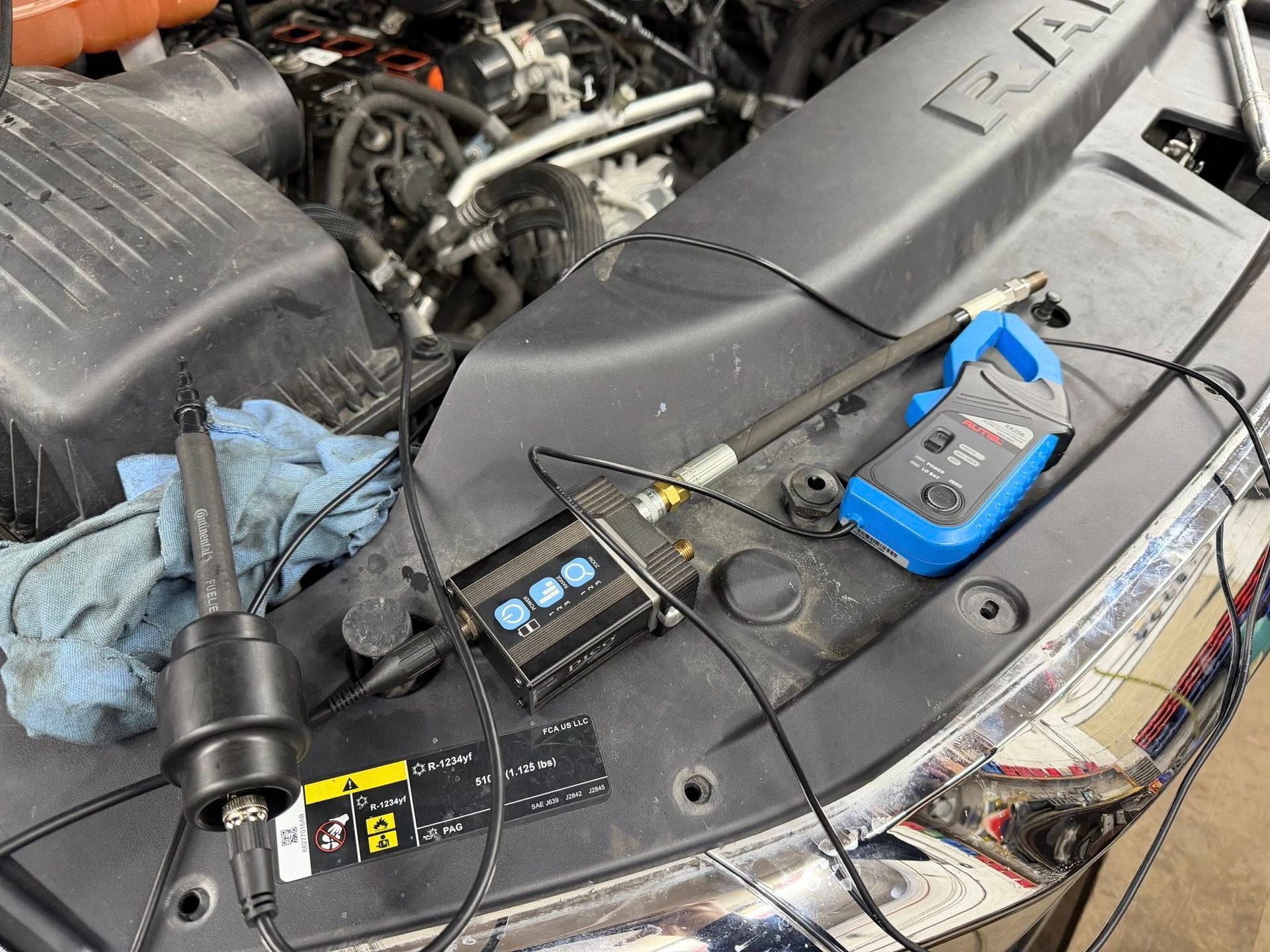 An open car hood with diagnostic tools laid out, testing an engine.
