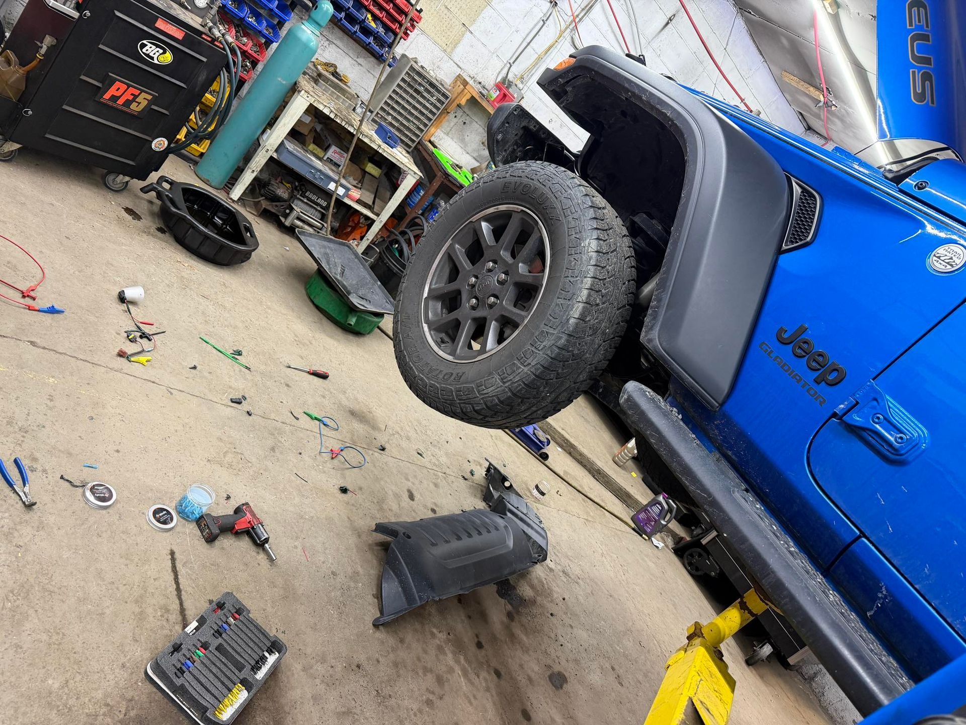 Blue Jeep Wrangler in a repair shop with tools and removed parts.
