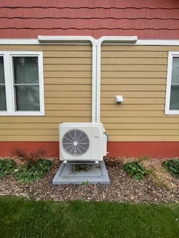A white air conditioner is sitting on the side of a house next to a window.