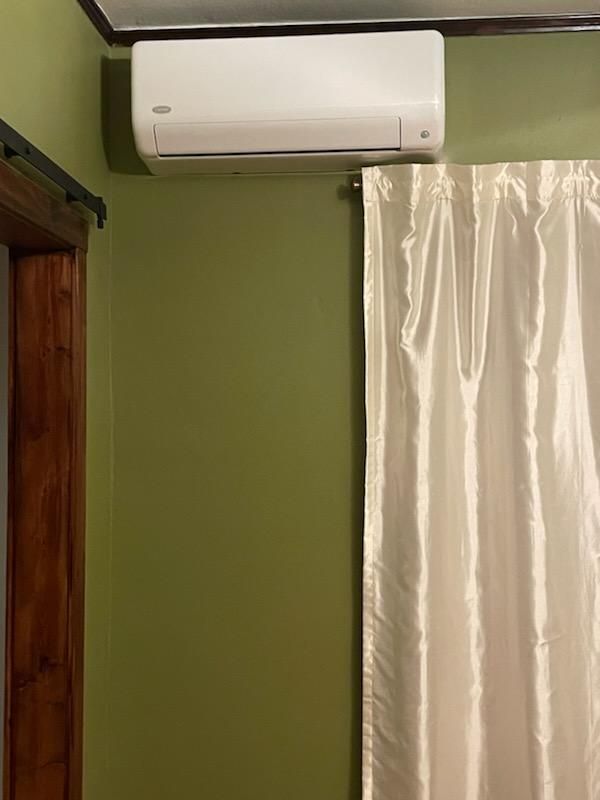A room with green walls and a white curtain and a white air conditioner hanging from the ceiling.
