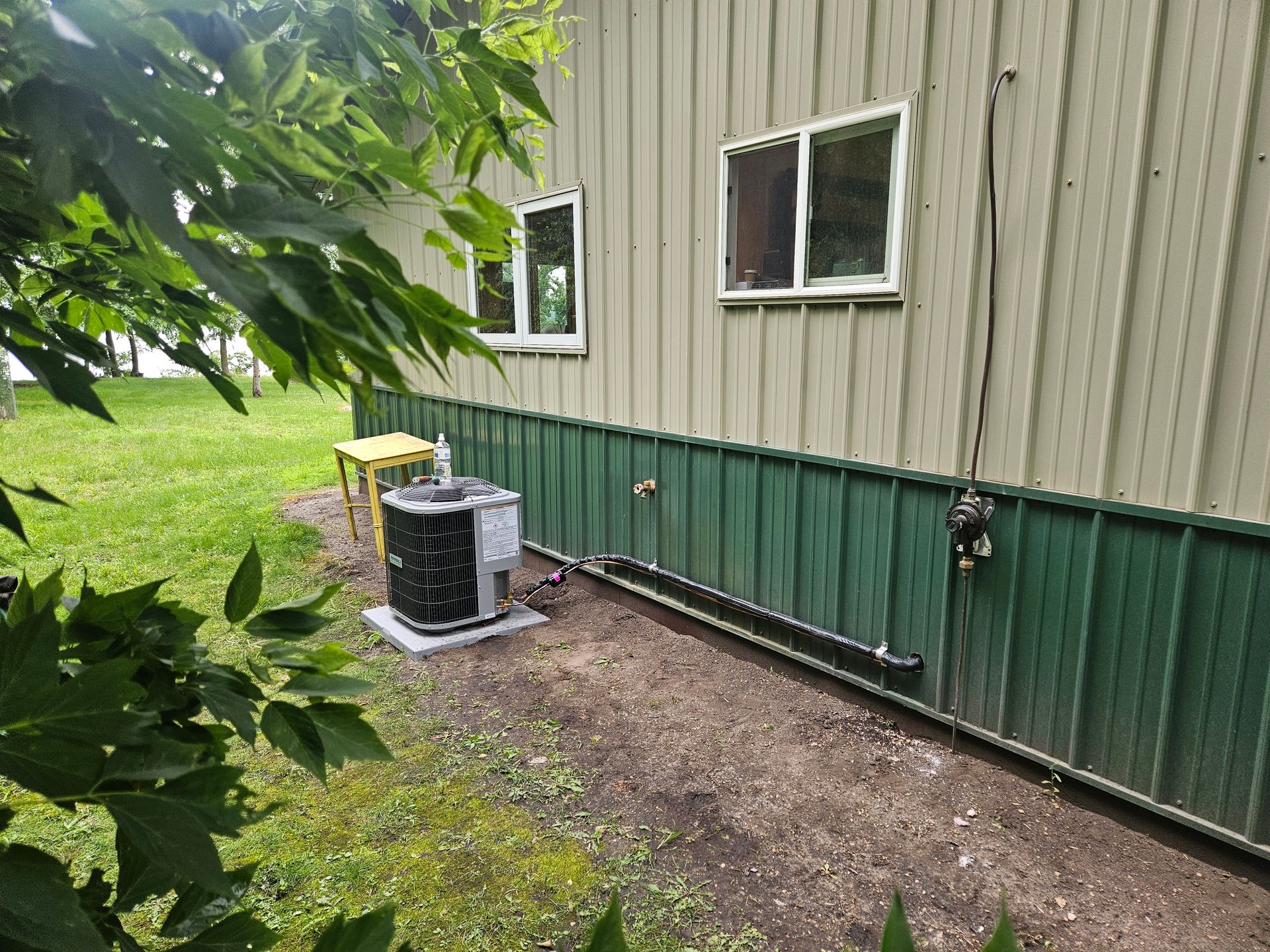 A house with a green siding and a air conditioner on the side of it.