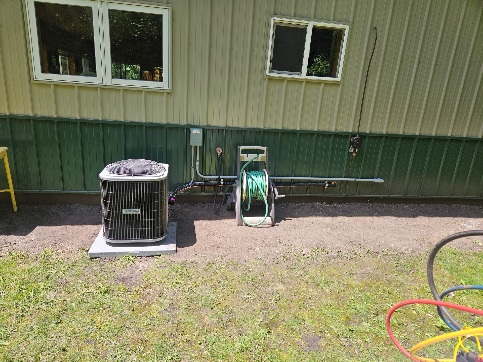 An air conditioner is sitting on the side of a building next to a hose.