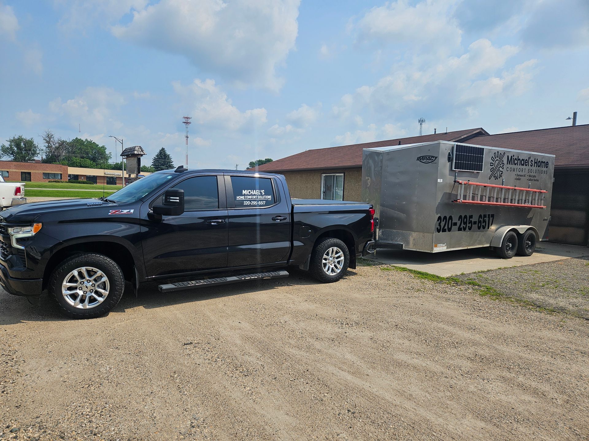 A black truck is towing a trailer in a gravel lot.