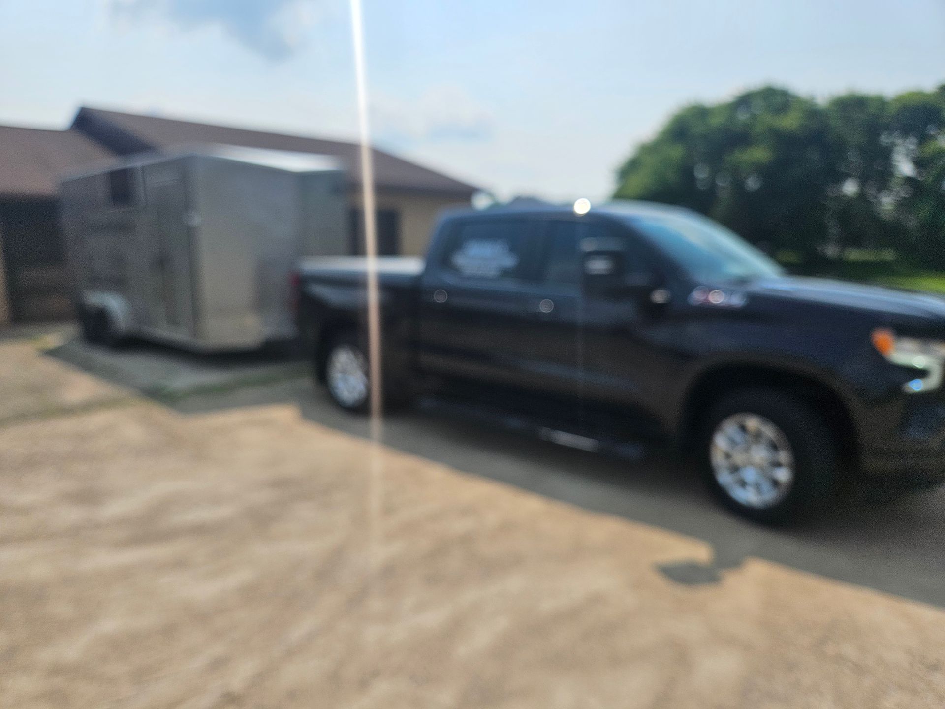 A black truck with a trailer attached to it is parked in front of a house.