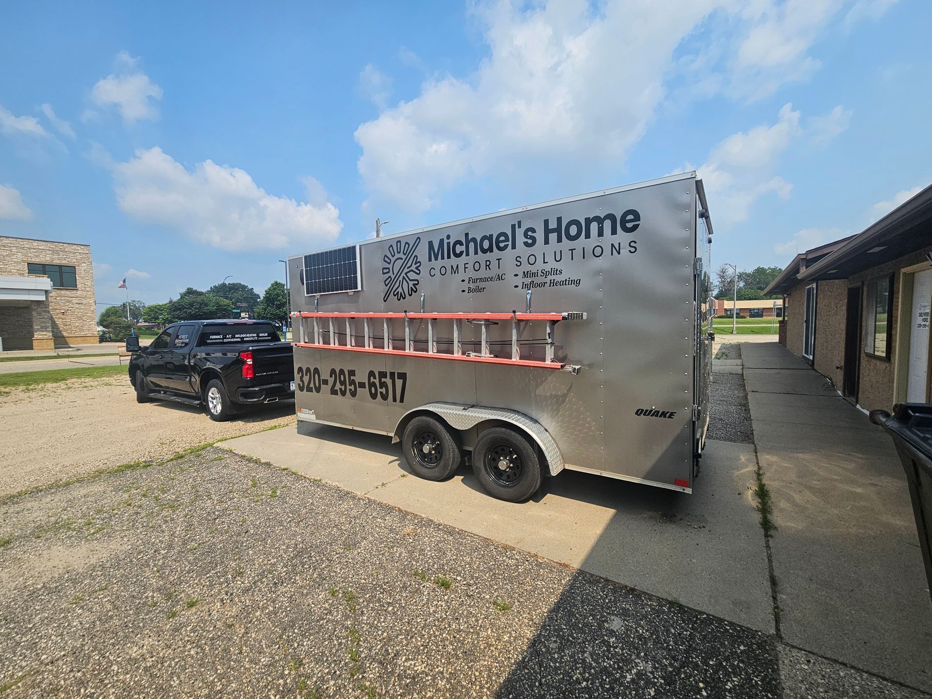 A trailer with a ladder attached to it is parked next to a truck.