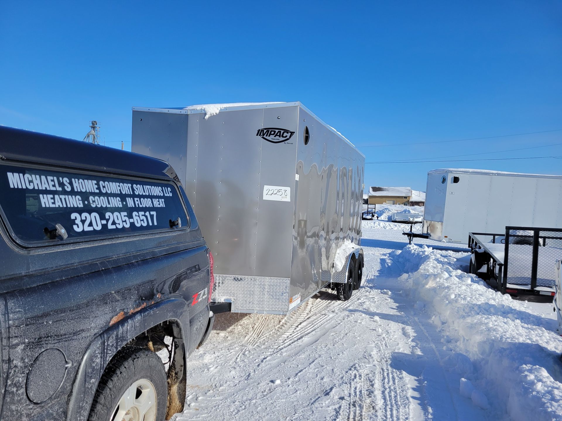 A truck is parked next to a trailer in the snow.