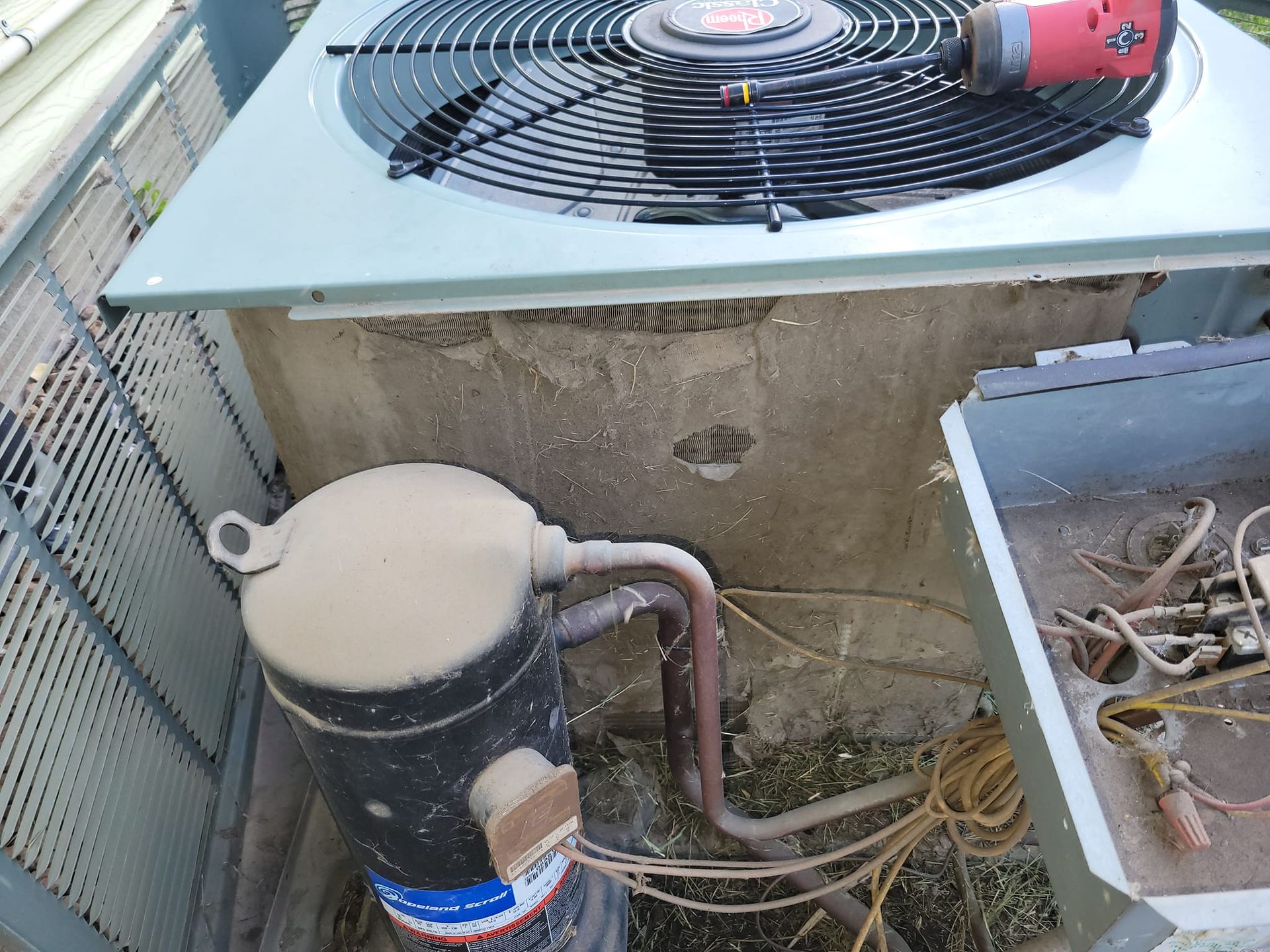 A dirty air conditioner with a drill on top of it.