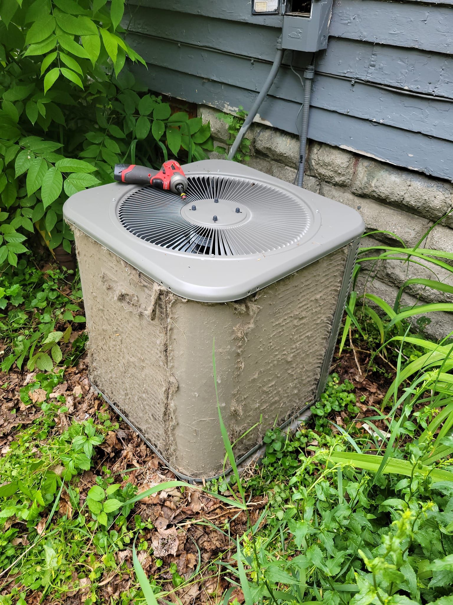 A dirty air conditioner is sitting in the grass next to a house.