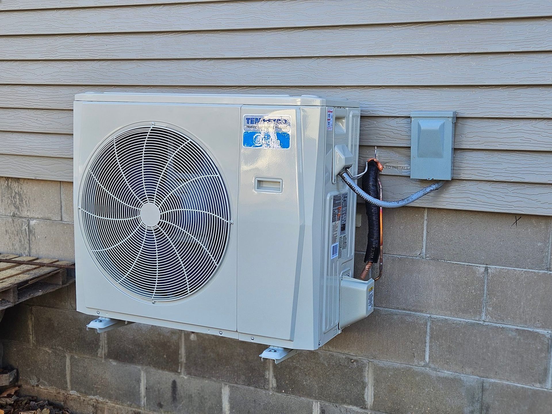 A white air conditioner is mounted on the side of a brick building.