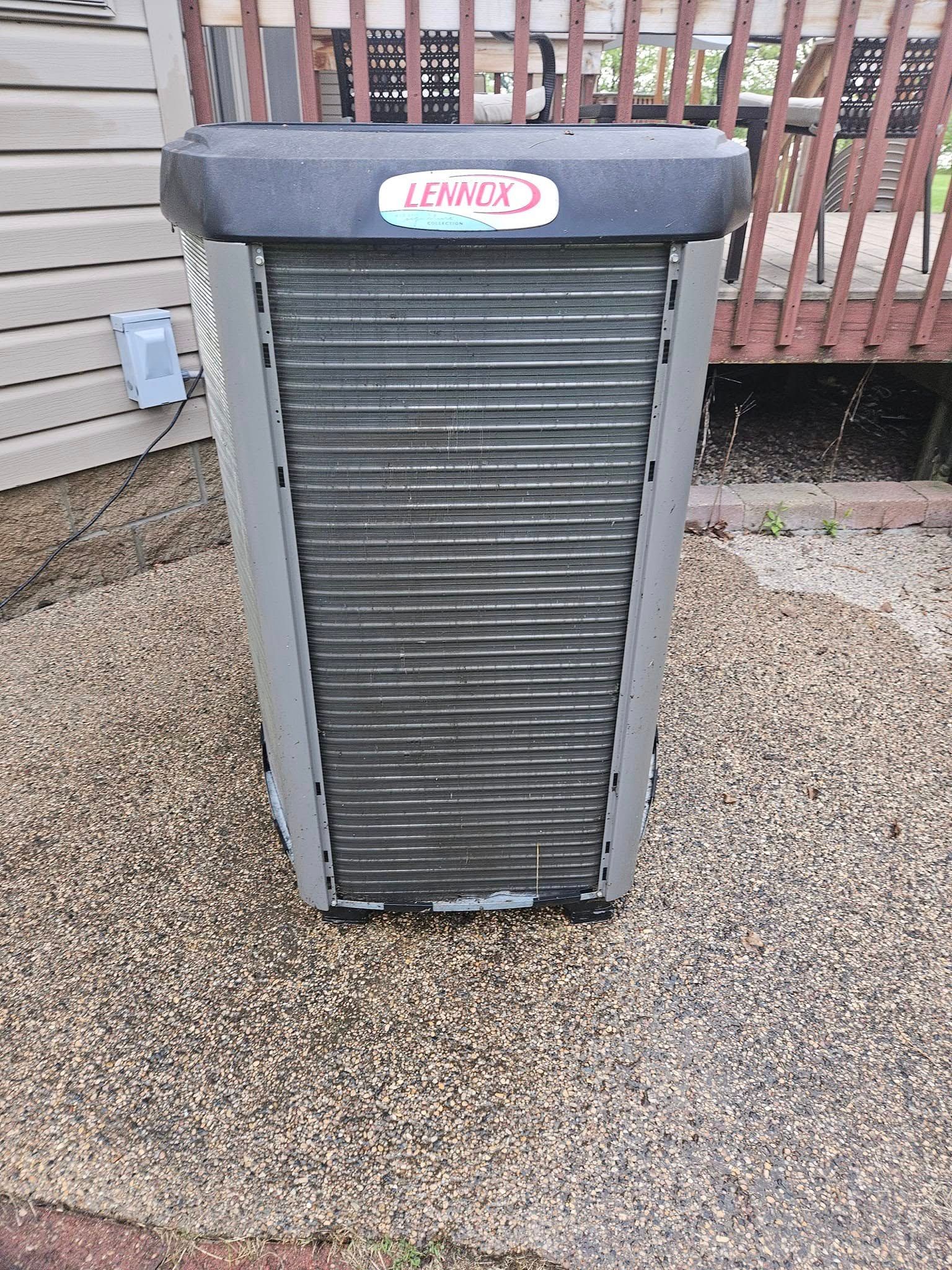 A large air conditioner is sitting on top of a gravel driveway next to a house.