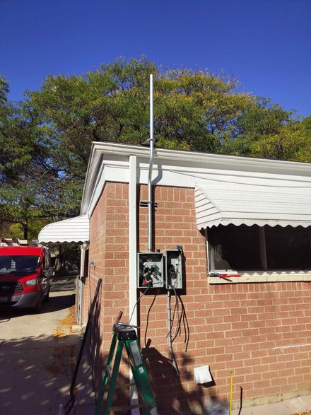 Brick building with utility meter, tall pole, red vehicle, and awning under a clear blue sky.