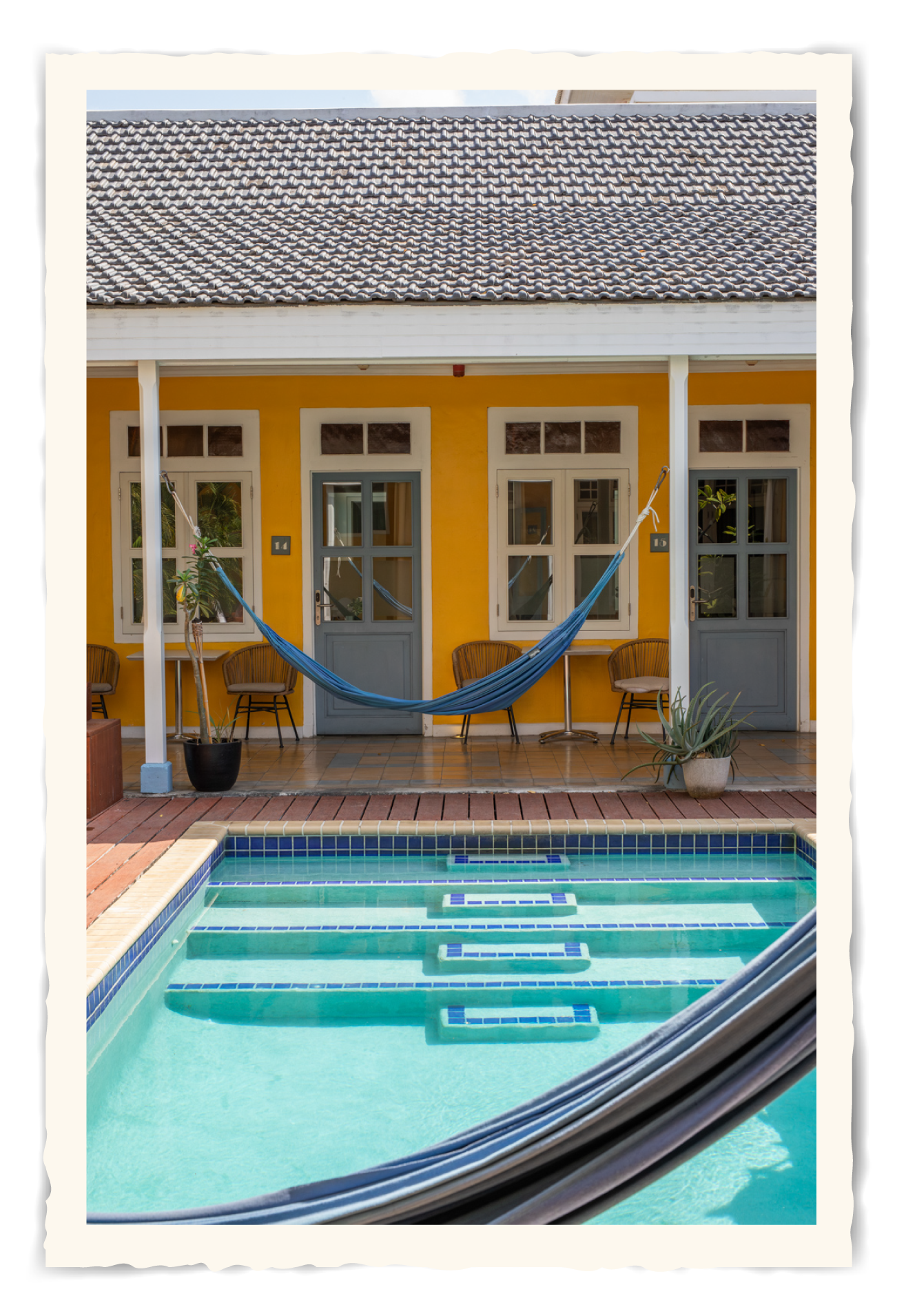 A yellow house with a swimming pool and a hammock t Klooster Hotel Curacao