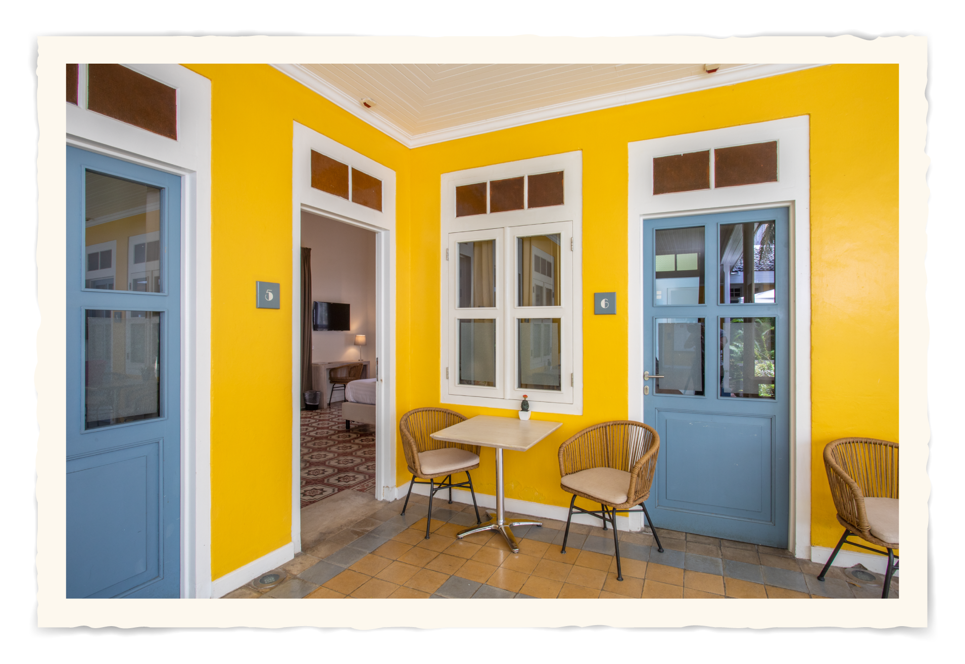 A room with yellow walls and blue doors has a table and chairs.