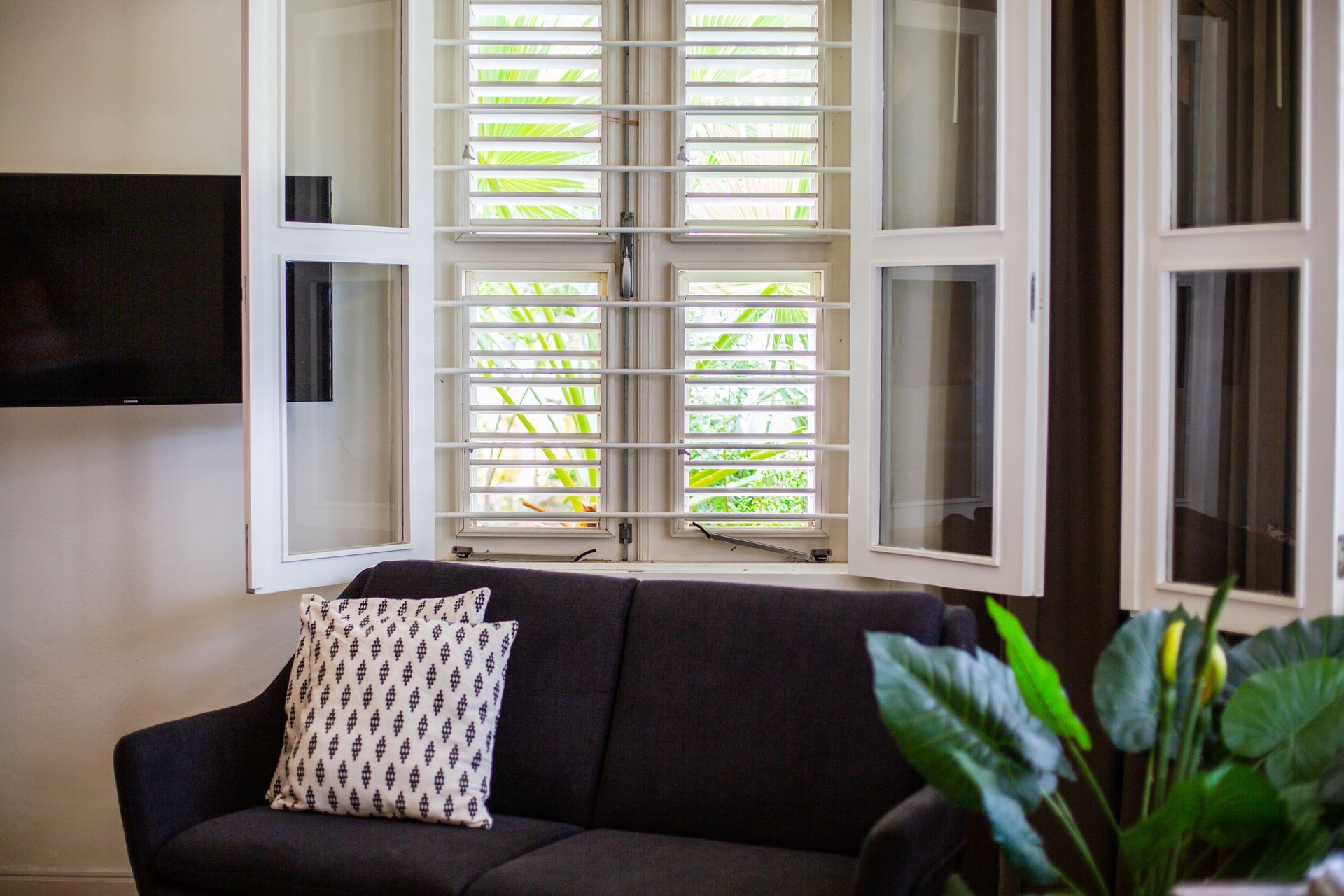 A living room with a couch , television , and shutters on the windows. t Klooster Hotel Curacao