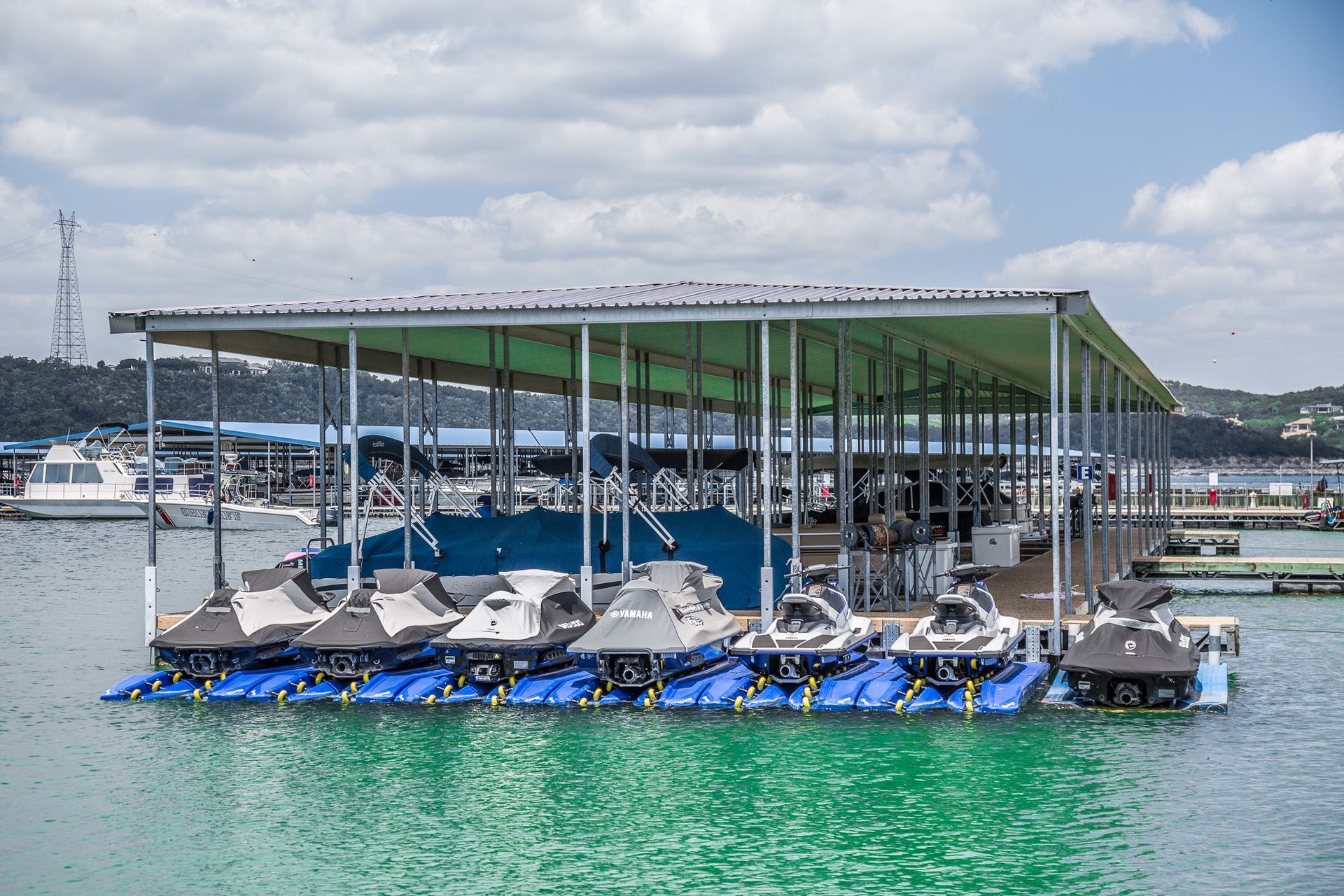 Jet skis docked on a floating platform under a covered structure at a marina with green water.