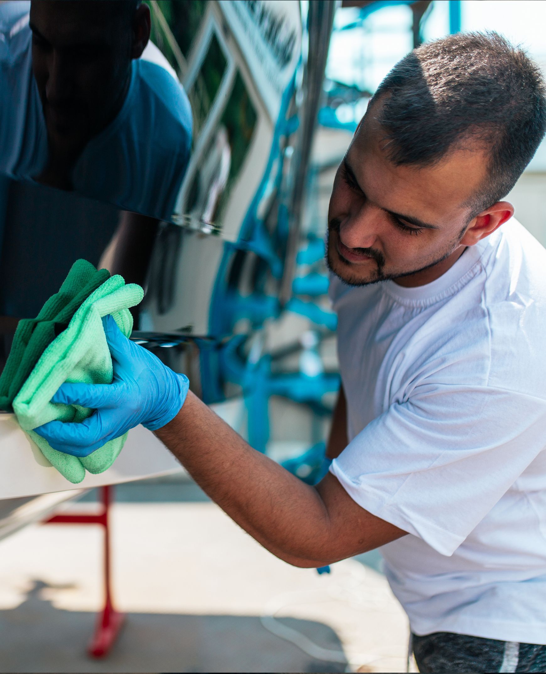 A man wearing blue gloves is cleaning a boat with a green cloth