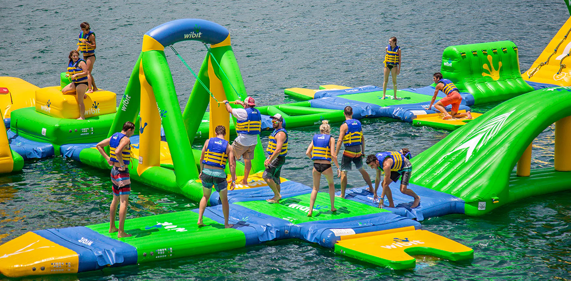 People playing on an inflatable water park in a lake, wearing life vests.