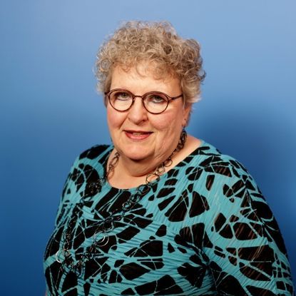 A woman wearing glasses and a blue shirt is smiling for the camera