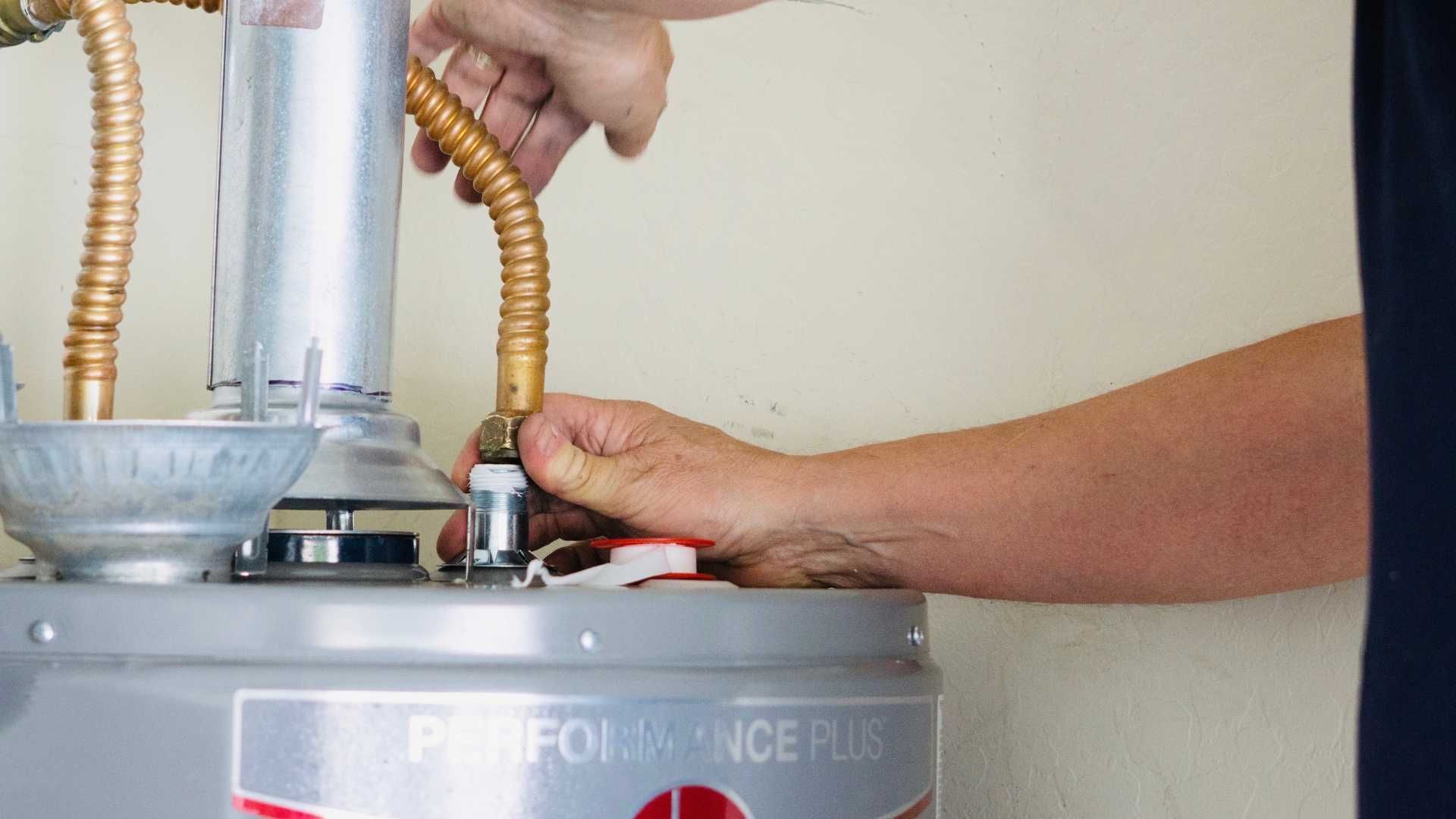 A person is fixing a water heater with a wrench.