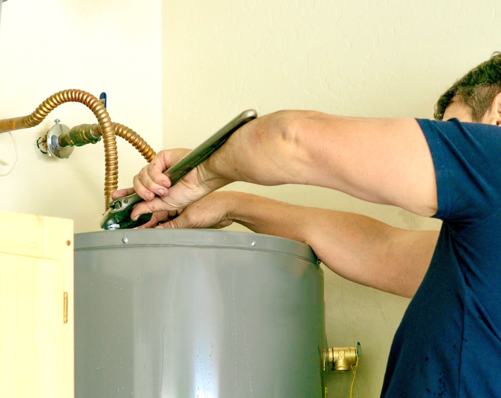 Person working on the top of a gray water heater with tools and hoses attached