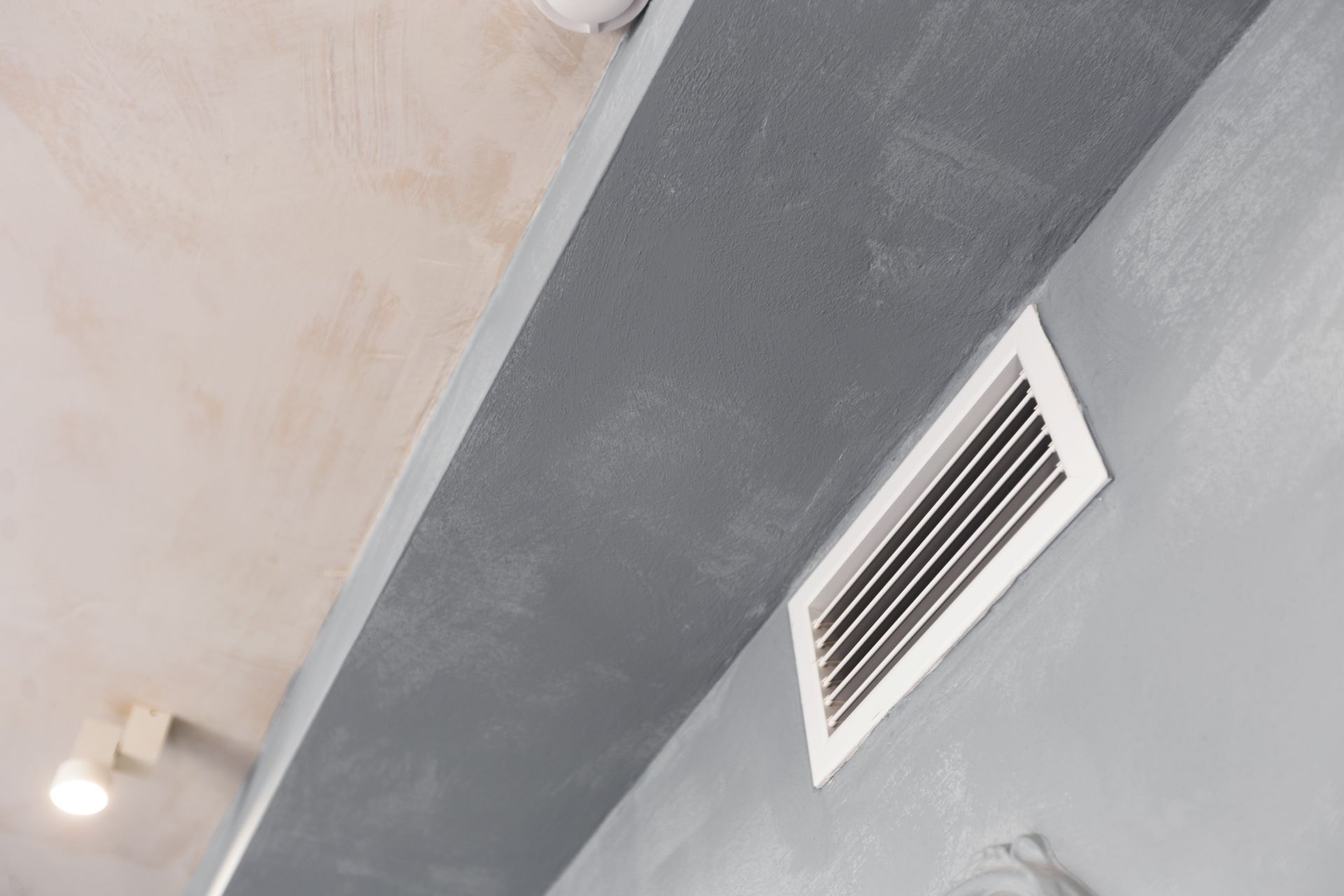 Gray wall and ceiling with a rectangular vent and recessed light fixture.